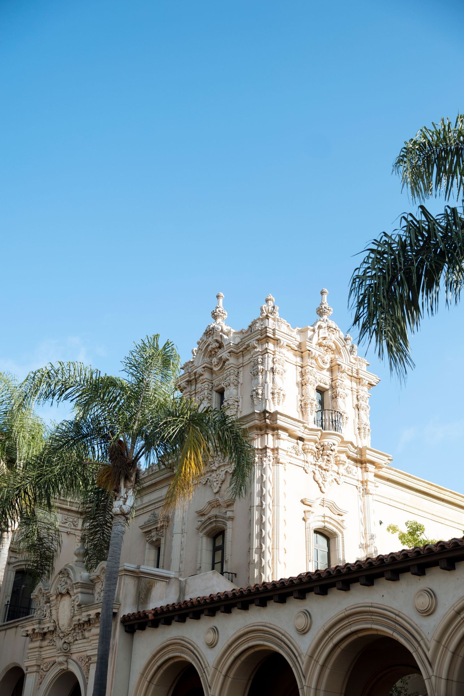 Spanish colonial architecture with ornate white facade and palm trees against bright blue sky at Balboa Park.