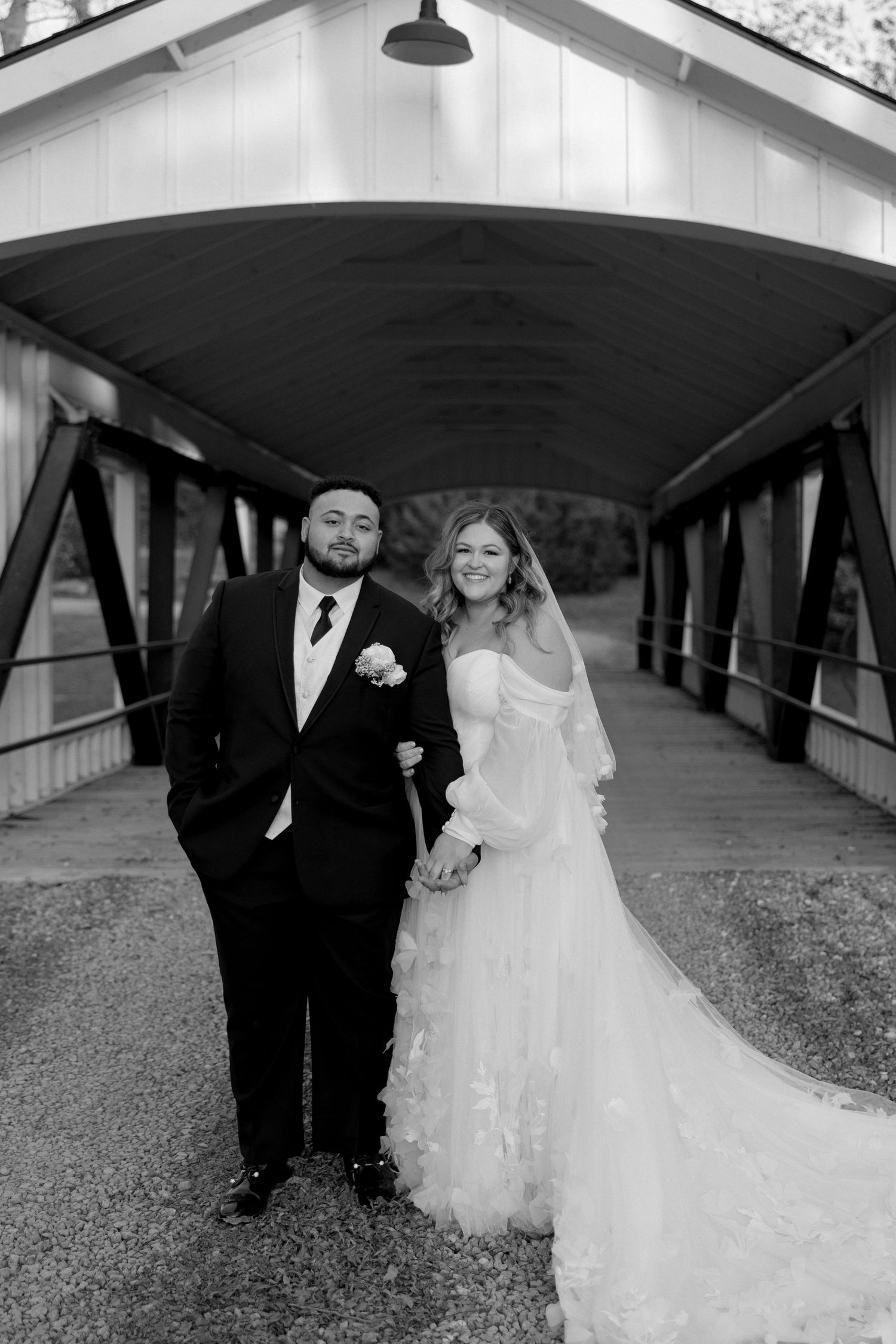 A black and white wedding portrait under covered bridge with classic composition.