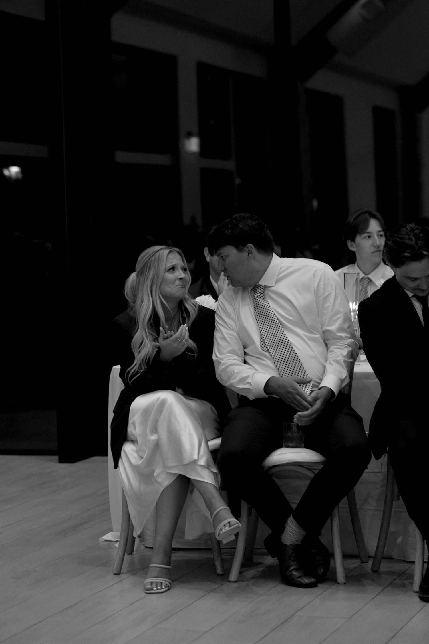 Black and white photo of wedding guests sitting and conversing in formal attire.