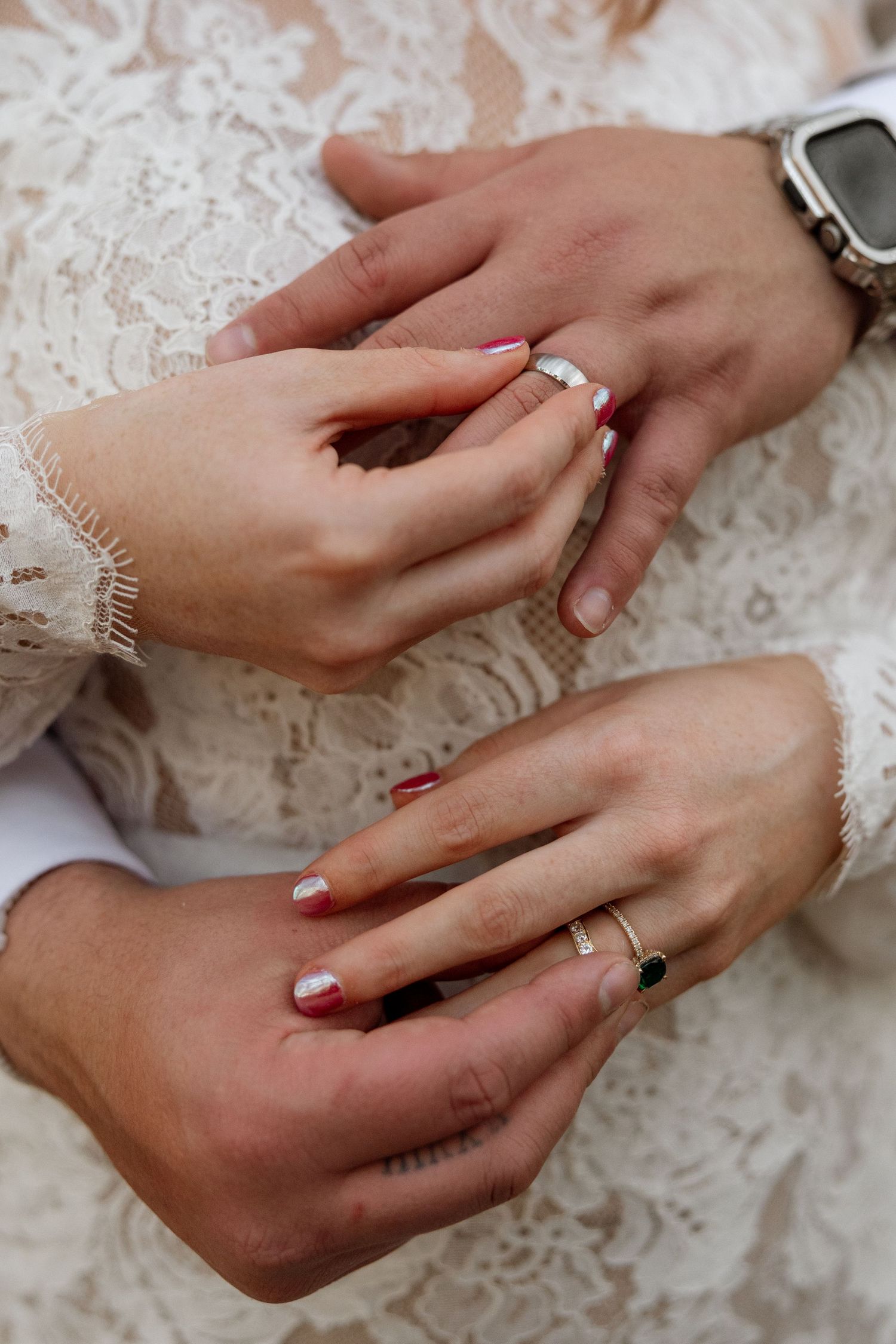 Close-up of hands exchanging rings with delicate lace details and manicured nails.