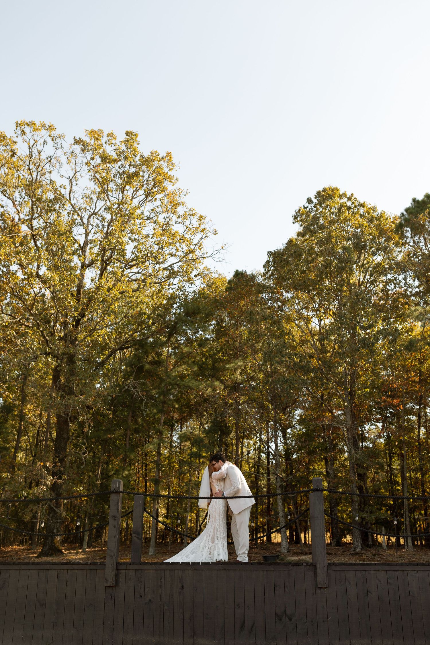 Distant view of newlyweds standing on elevated deck surrounded by fall foliage.