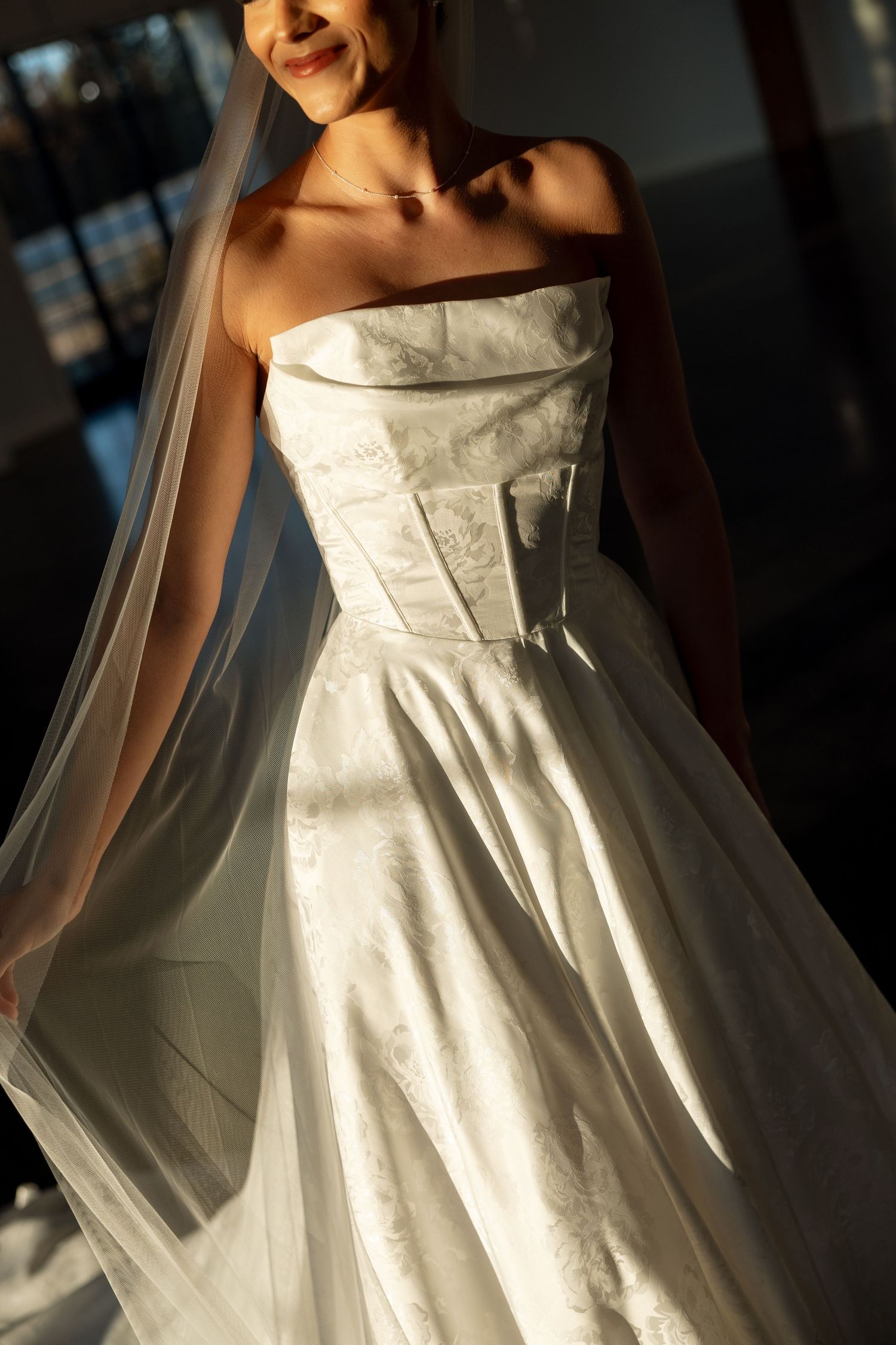 Sunlight streams through windows onto a strapless wedding dress with structured bodice and full skirt.