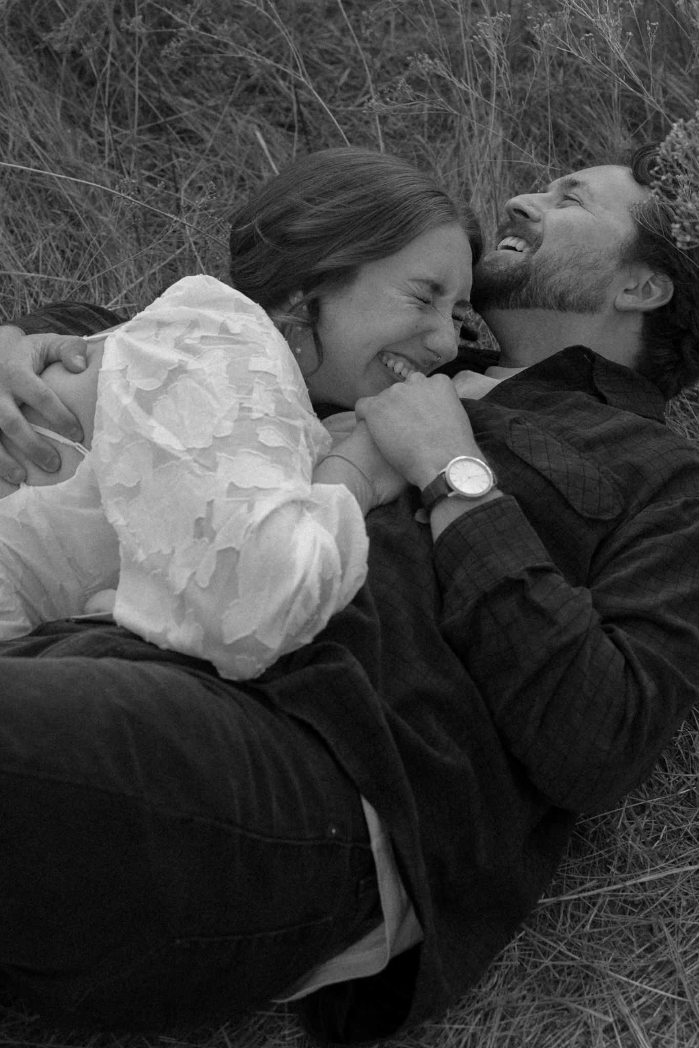 A candid black and white photo shows a joyful couple sharing laughter while lying outdoors.