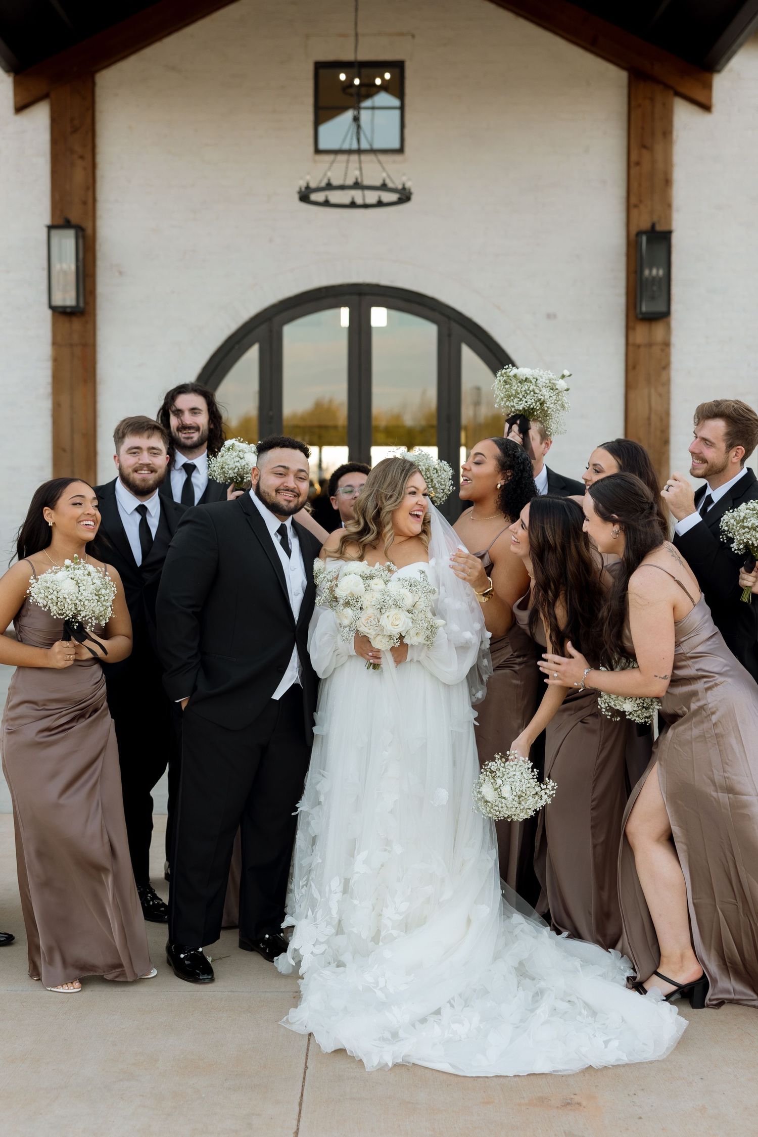 A joyful wedding party gathers for a group photo outside their venue.