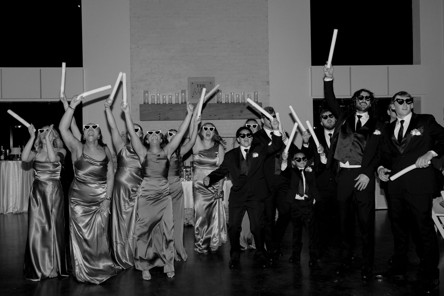 Black and white photo of wedding party dancing and celebrating with raised arms.