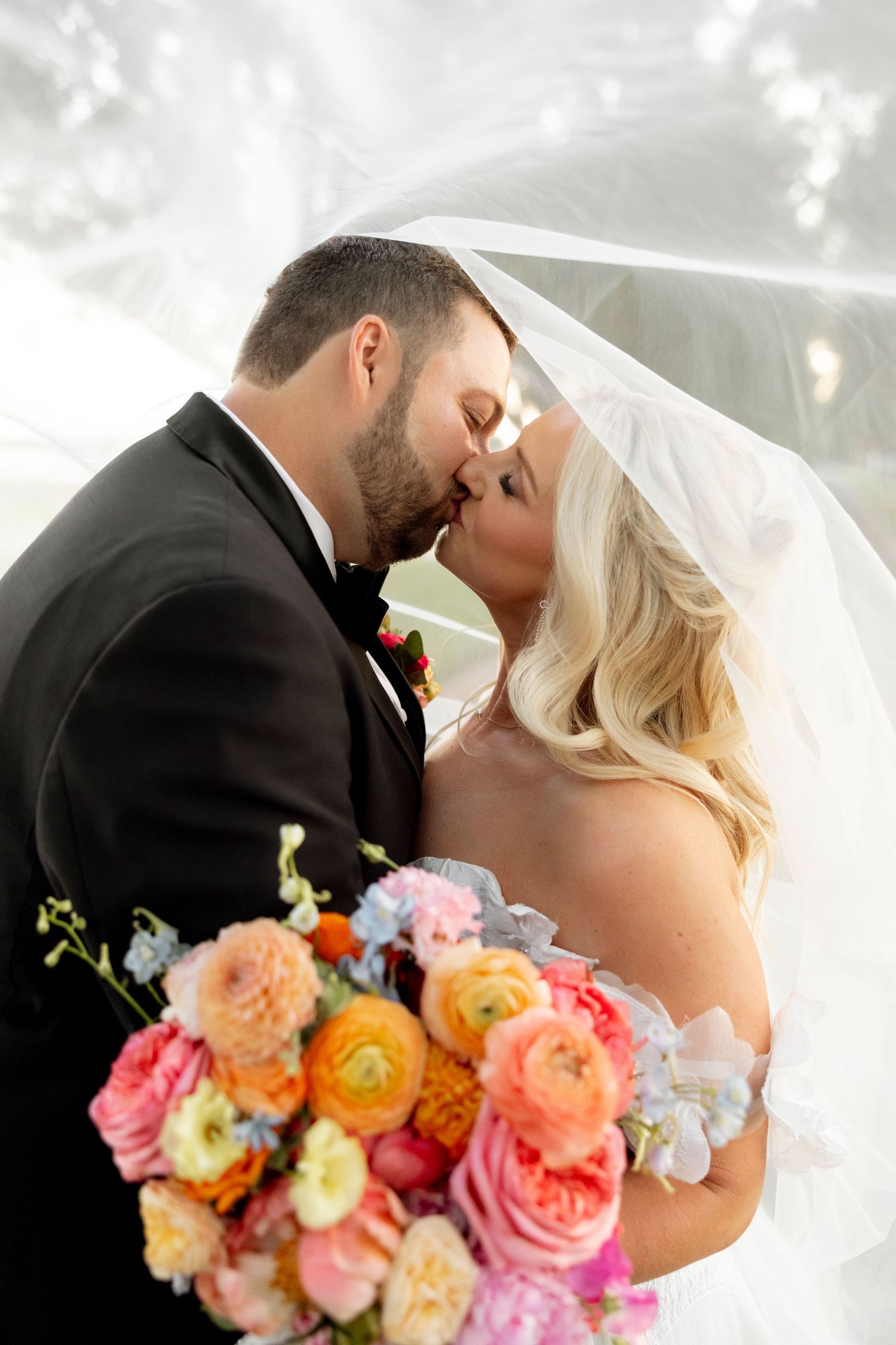 Romantic wedding portrait with soft lighting and colorful floral bouquet featuring coral and peach blooms.