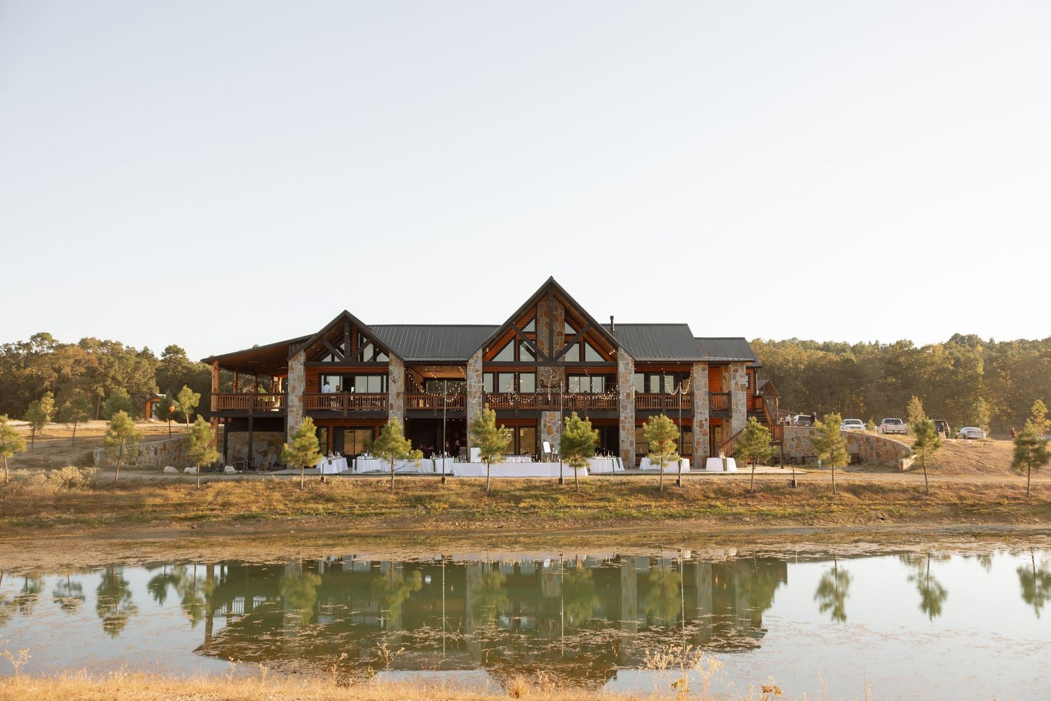 Large rustic lodge-style venue building reflected in a lake during golden hour.