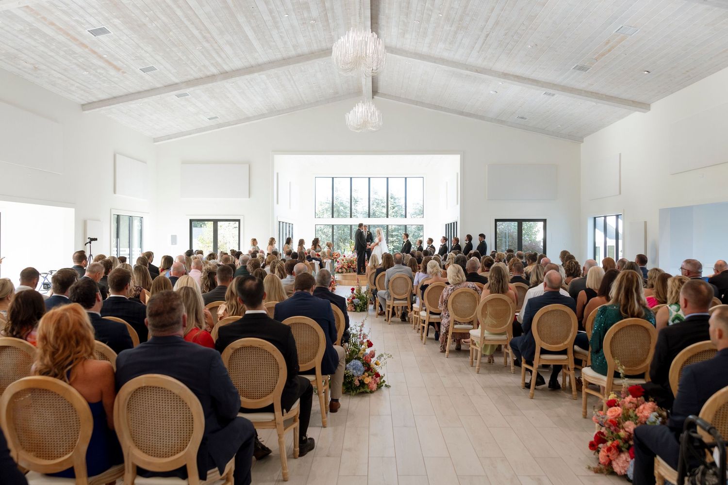 Wide view of wedding ceremony venue with rows of chairs filled with guests.