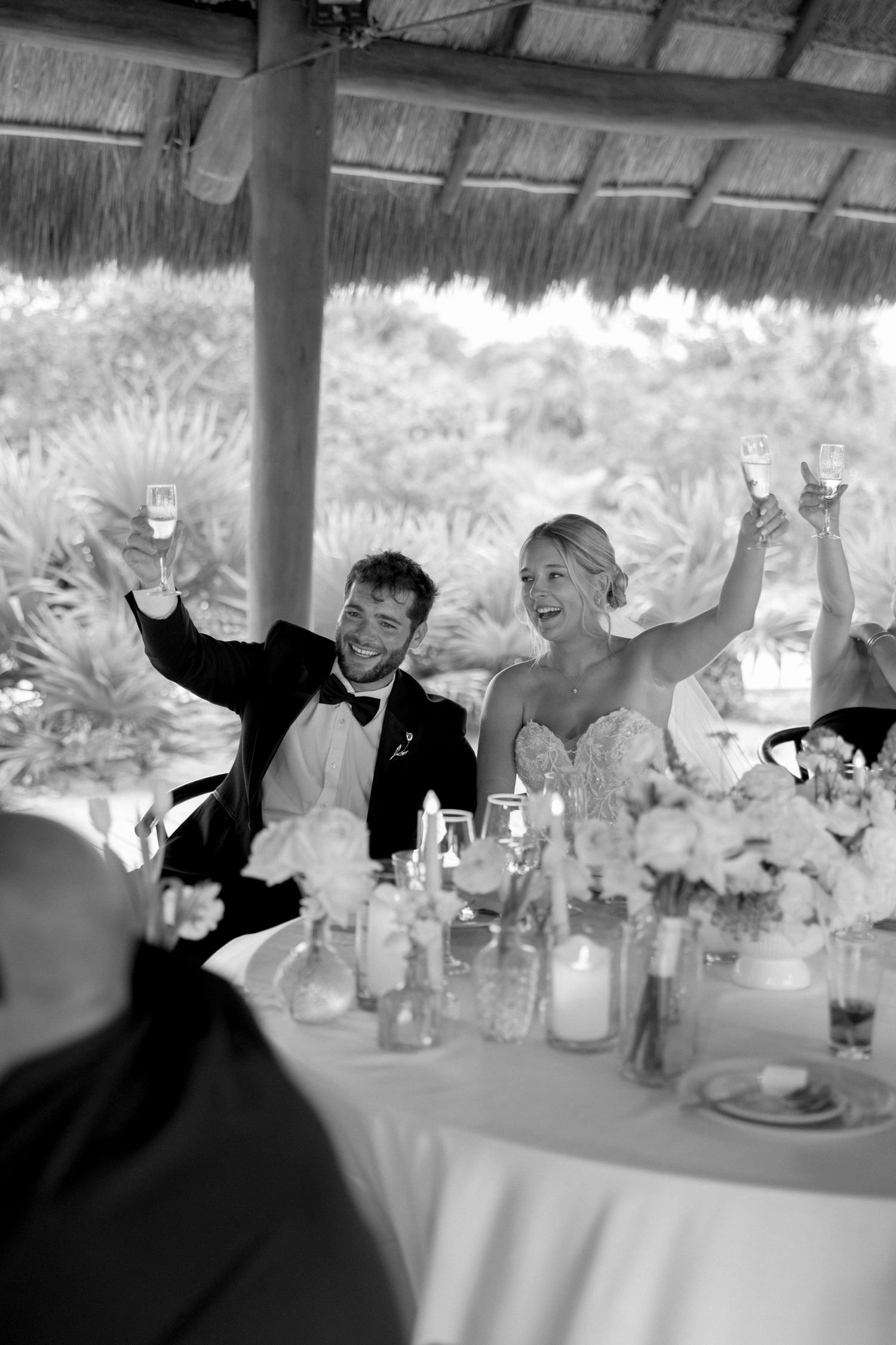 Wedding reception guests celebrating with raised arms at a covered outdoor venue.