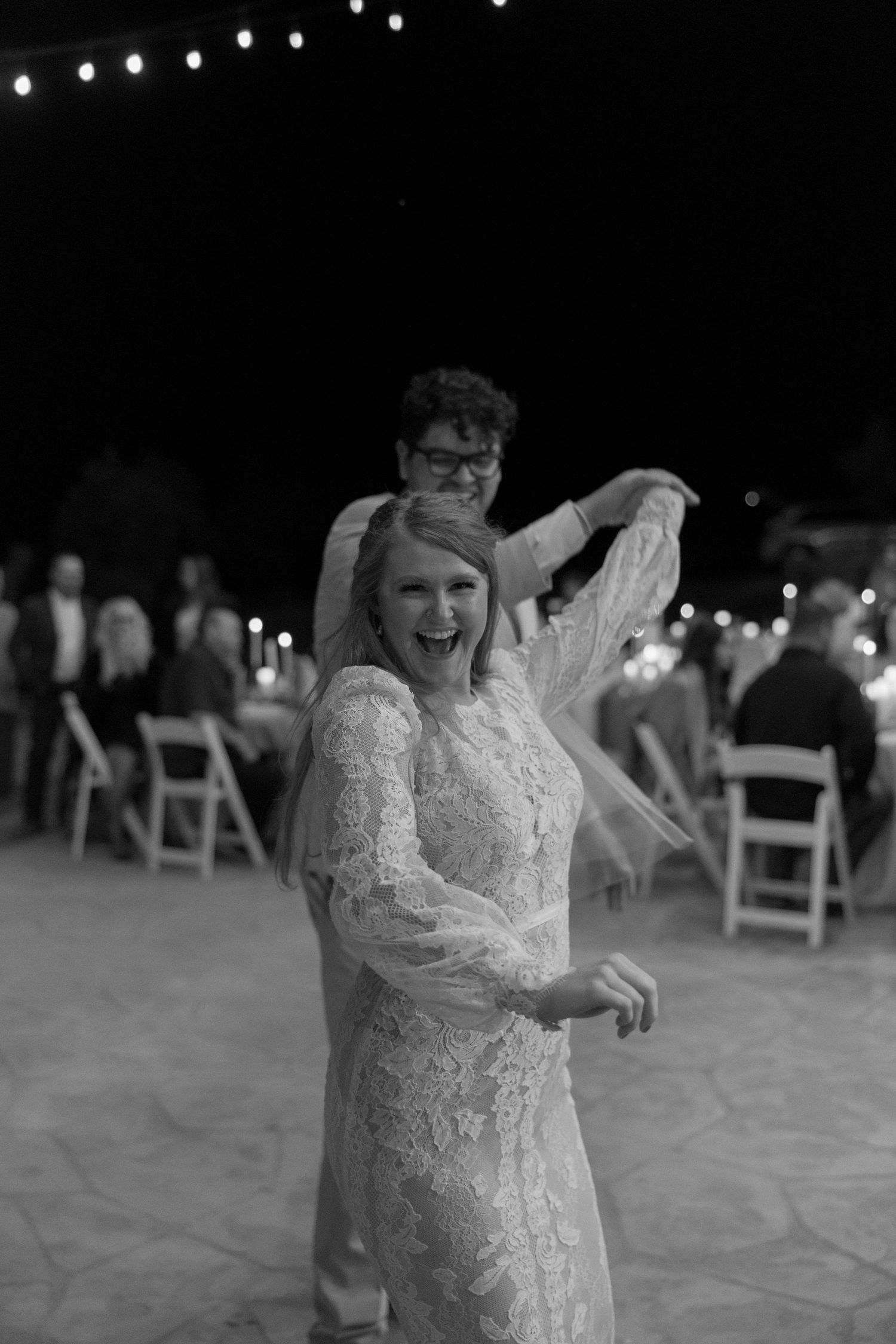 A playful black and white dance photo at an outdoor wedding reception.