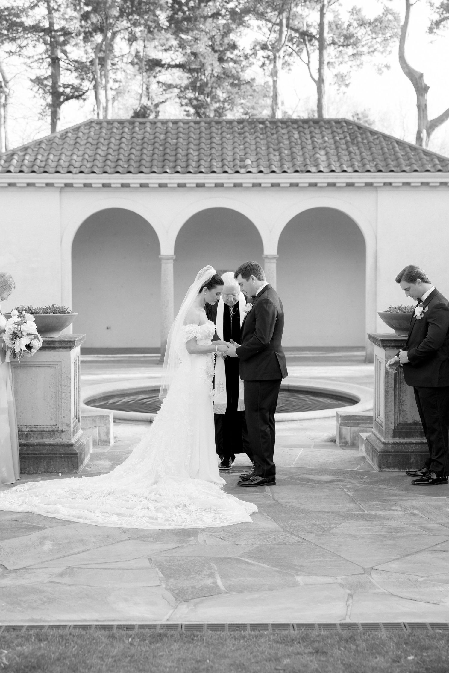 Black and white photo of bride and groom exchanging vows at an outdoor wedding ceremony.