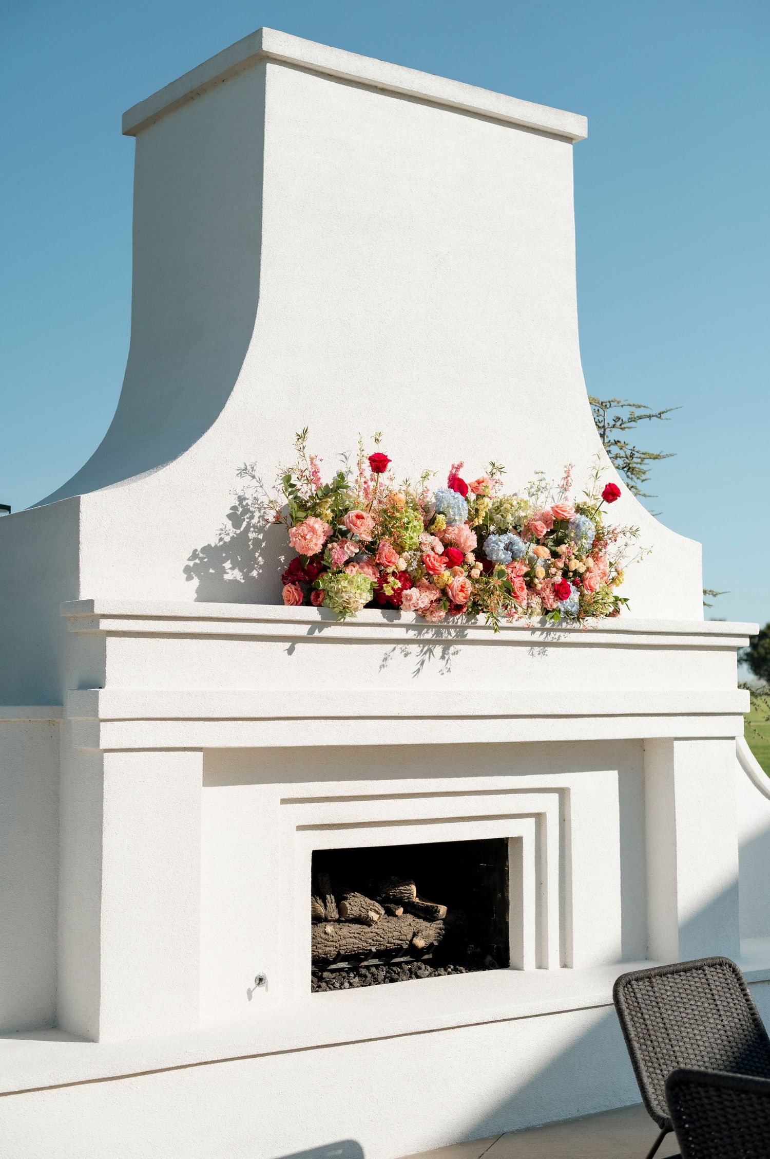 Modern white outdoor fireplace decorated with vibrant coral and pink floral arrangements.