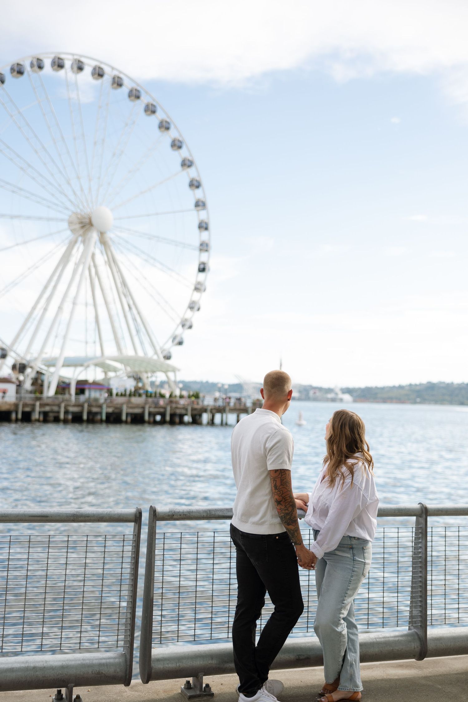Couple enjoying waterfront view with Seattle Great Wheel on sunny day.