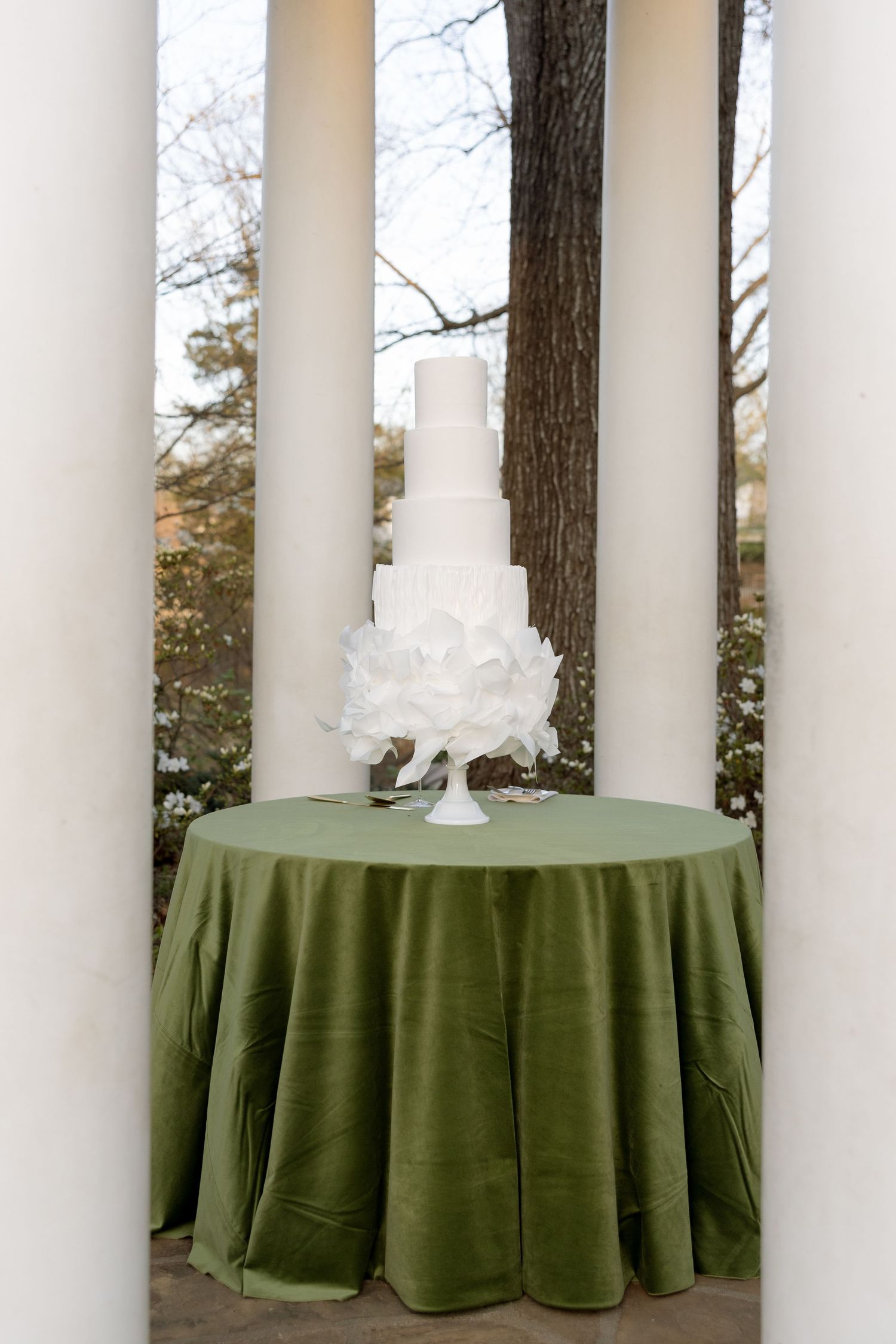 Elegant four-tier white wedding cake adorned with ruffled flowers displayed on a green velvet table.