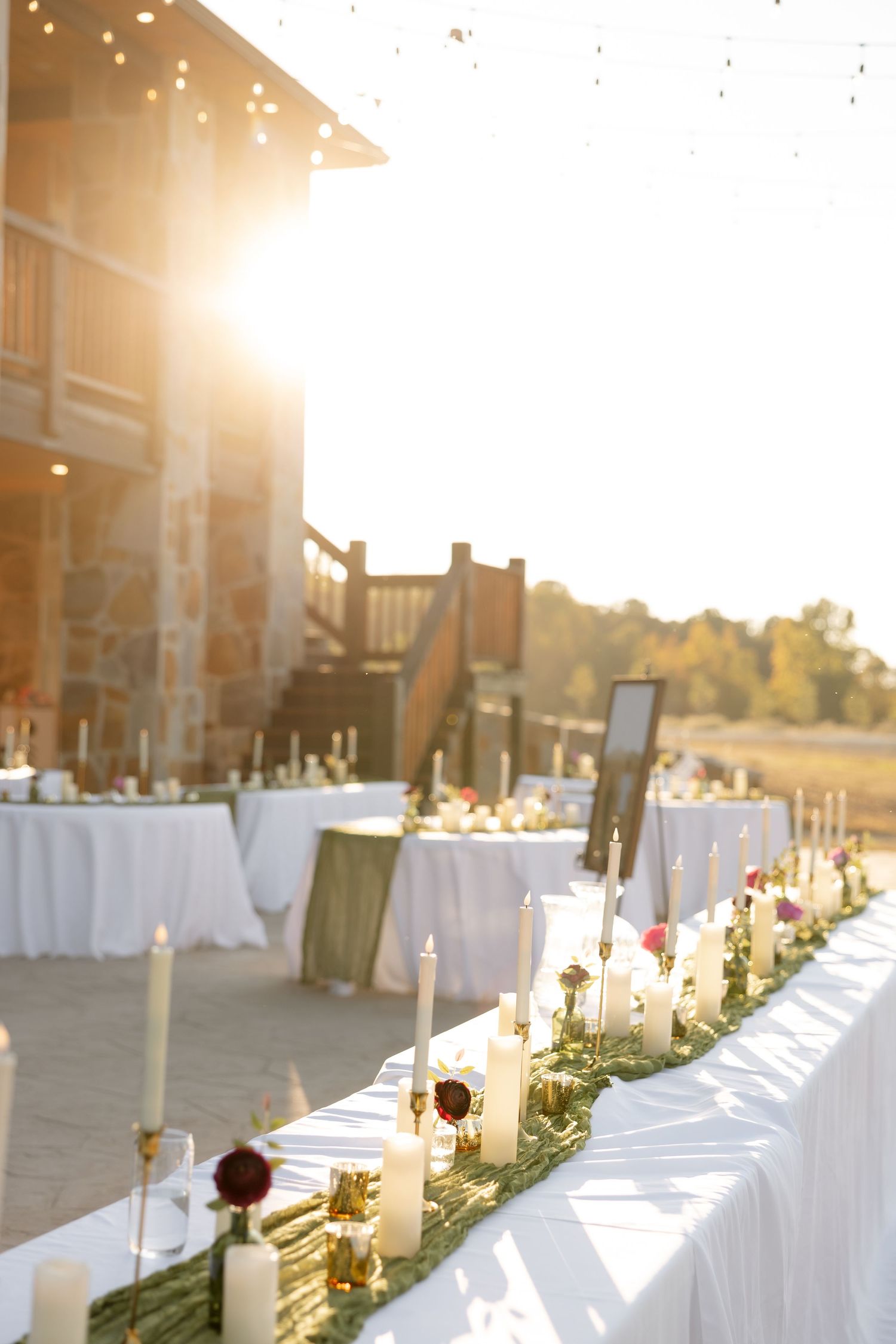 Reception tables decorated with white linens, candles and floral runners in golden sunset light.