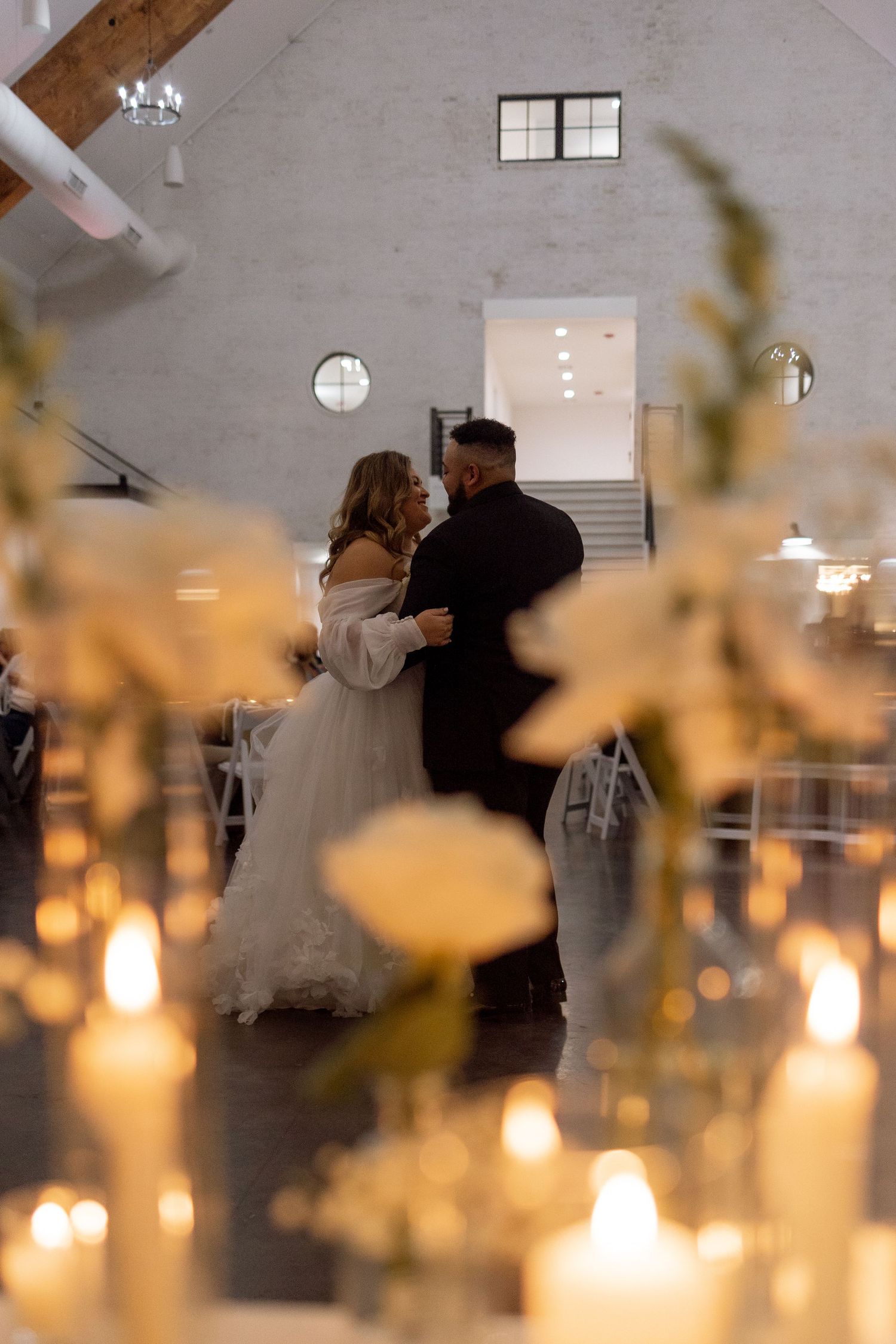 Couple shares intimate dance surrounded by glowing candles in modern reception space.