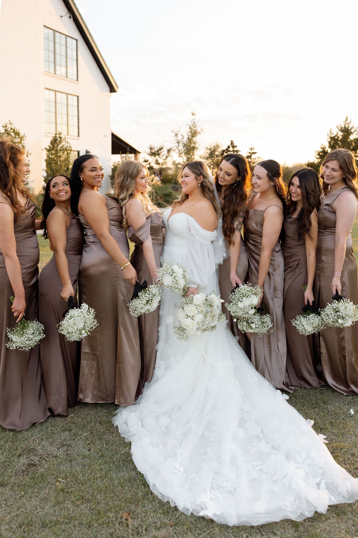 Bridal party poses together outdoors wearing mauve dresses with white floral bouquets.
