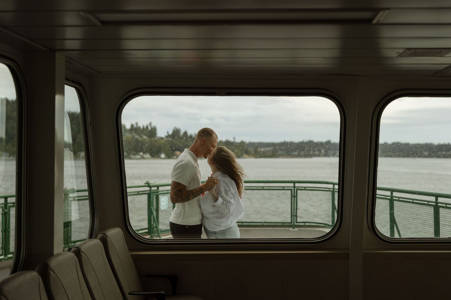 Through a boat window, a couple shares an intimate moment on the deck with scenic water views.