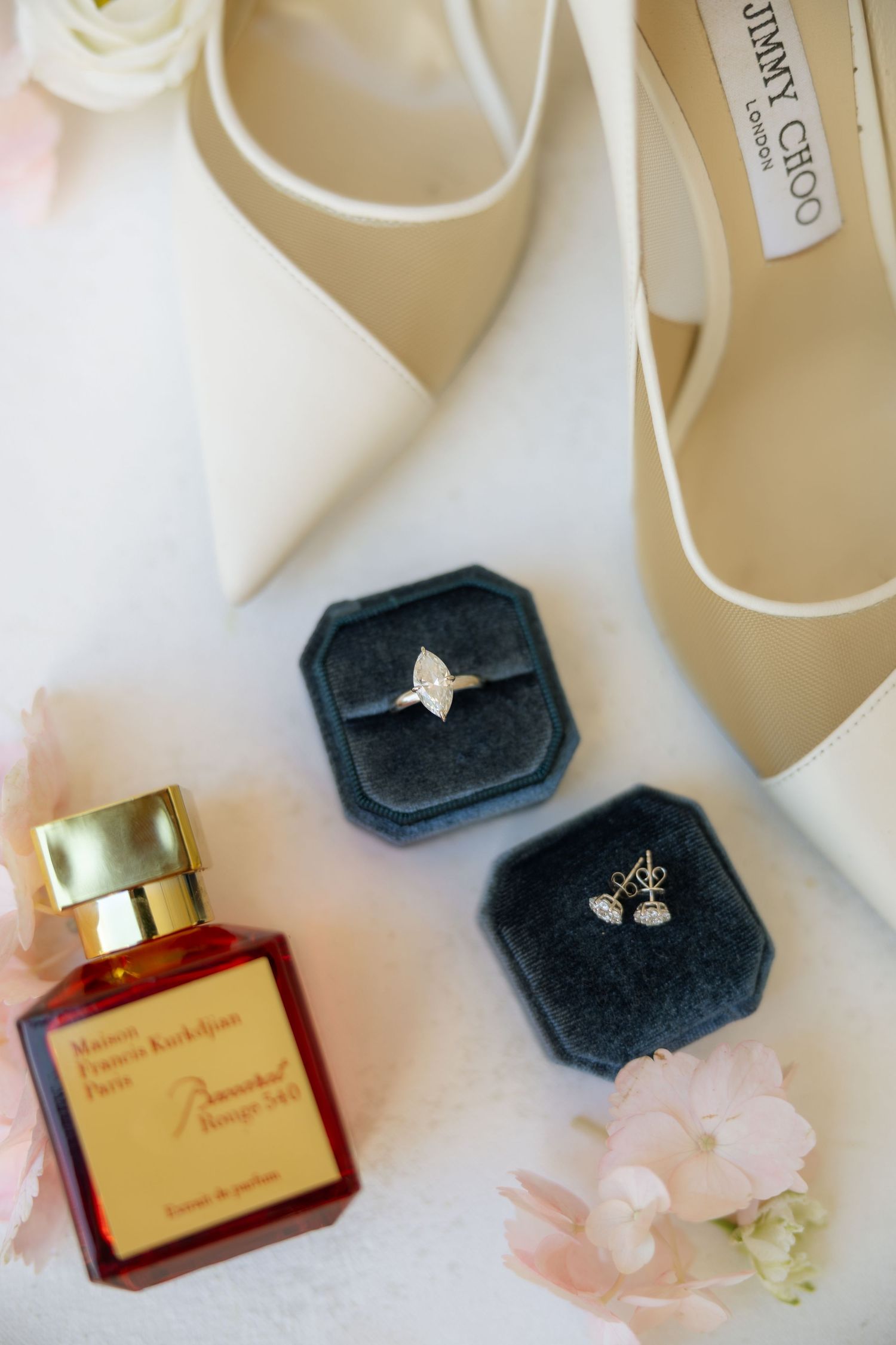 Wedding flat lay featuring diamond ring, earrings, Baccarat Rouge perfume, and Jimmy Choo heels.