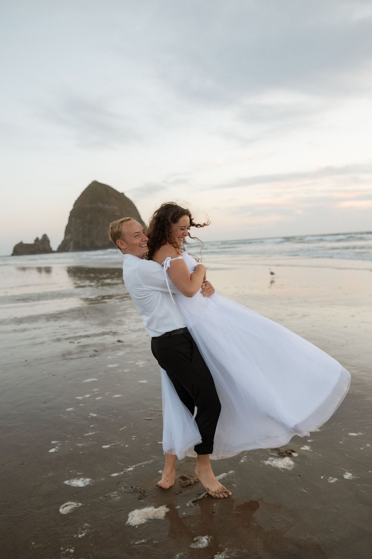 A romantic beachside embrace in front of Haystack Rock during a sunset wedding photoshoot.