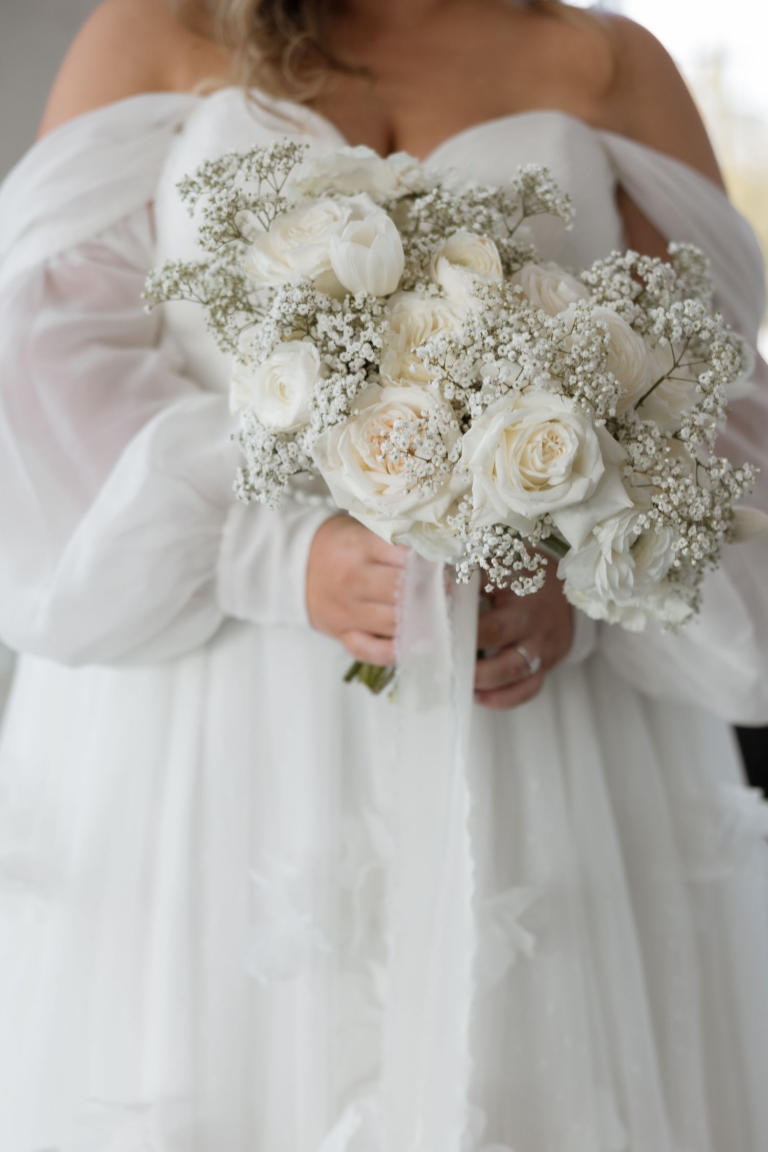 An elegant white bridal bouquet featuring roses and baby's breath against a flowing wedding dress.