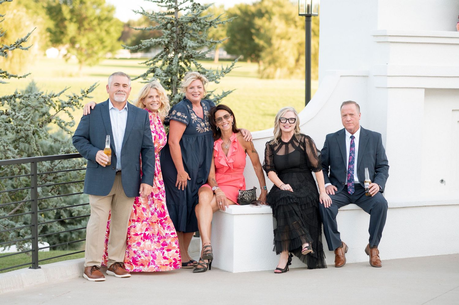 Wedding party poses together outdoors in front of a white building on a sunny day.