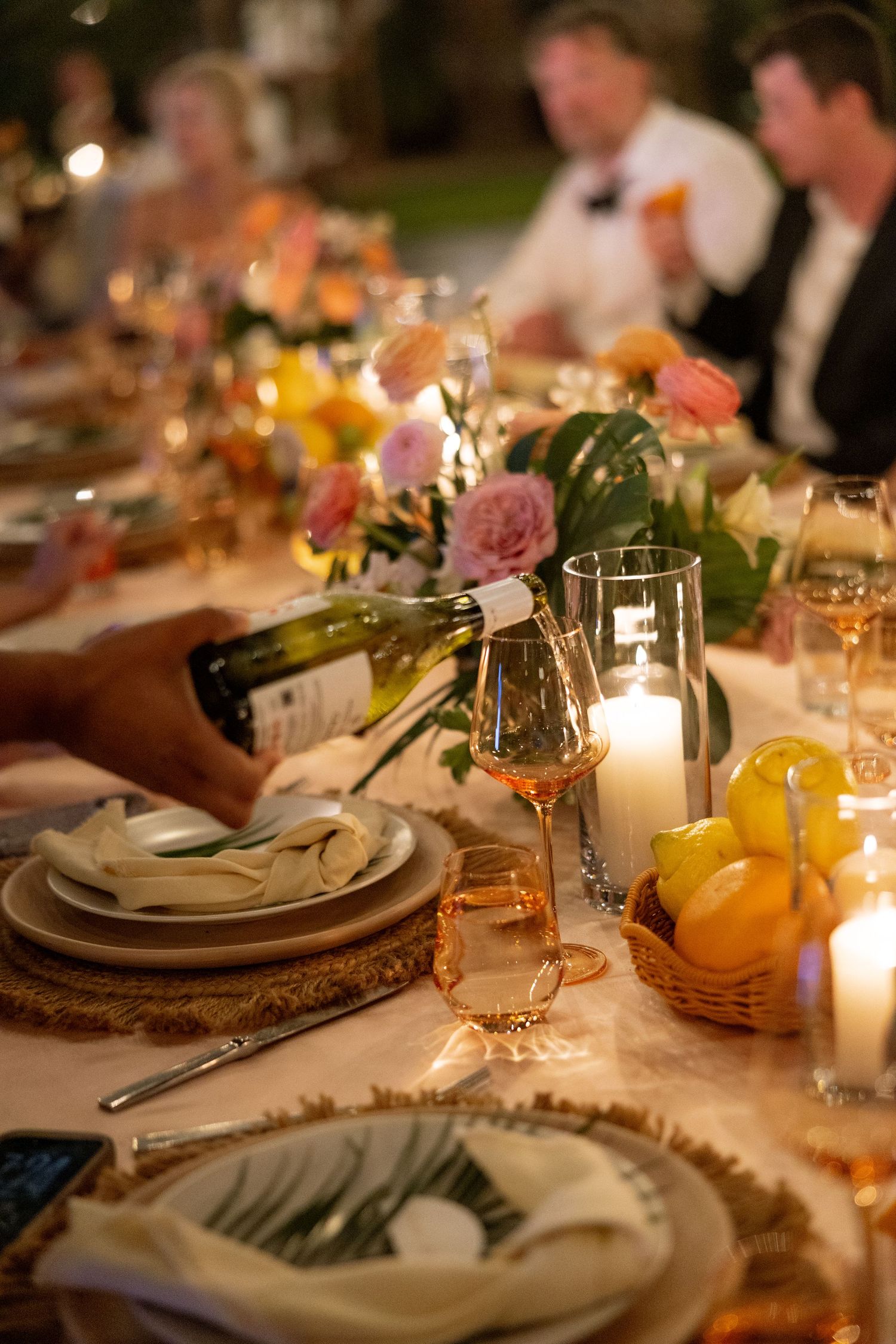 Wine being poured at an elegant candlelit wedding reception dinner table with floral centerpieces and citrus fruit decor.