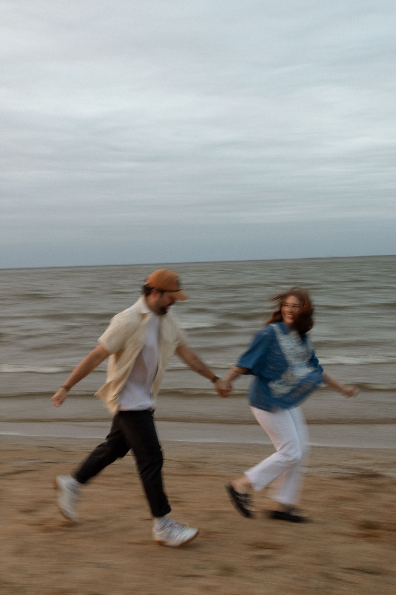 A couple enjoys a carefree moment running on the beach during an overcast day.