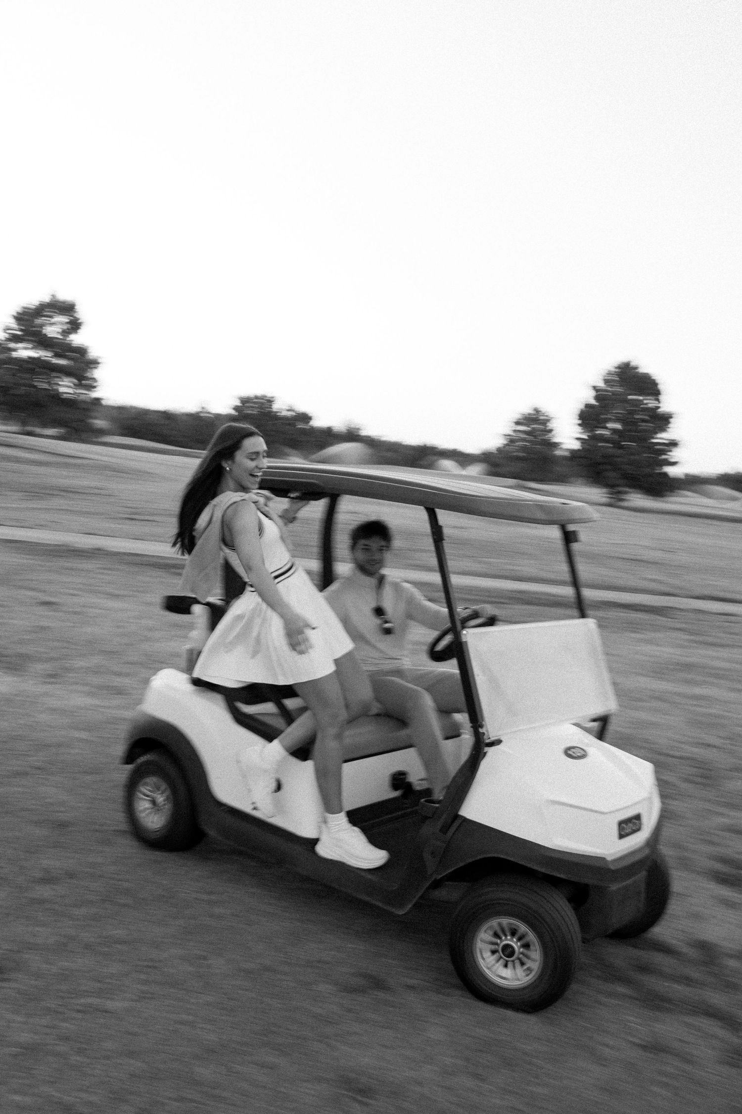 Black and white action shot of a couple riding in a golf cart across the course.