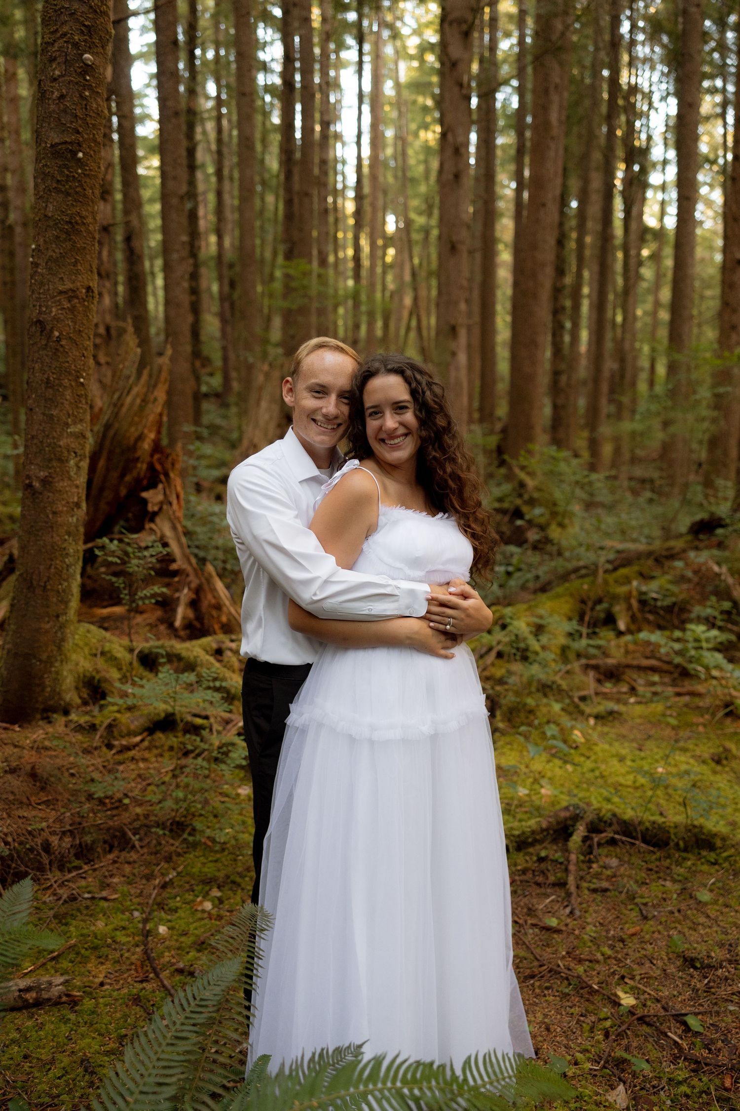 A romantic wedding portrait in a lush evergreen forest setting.