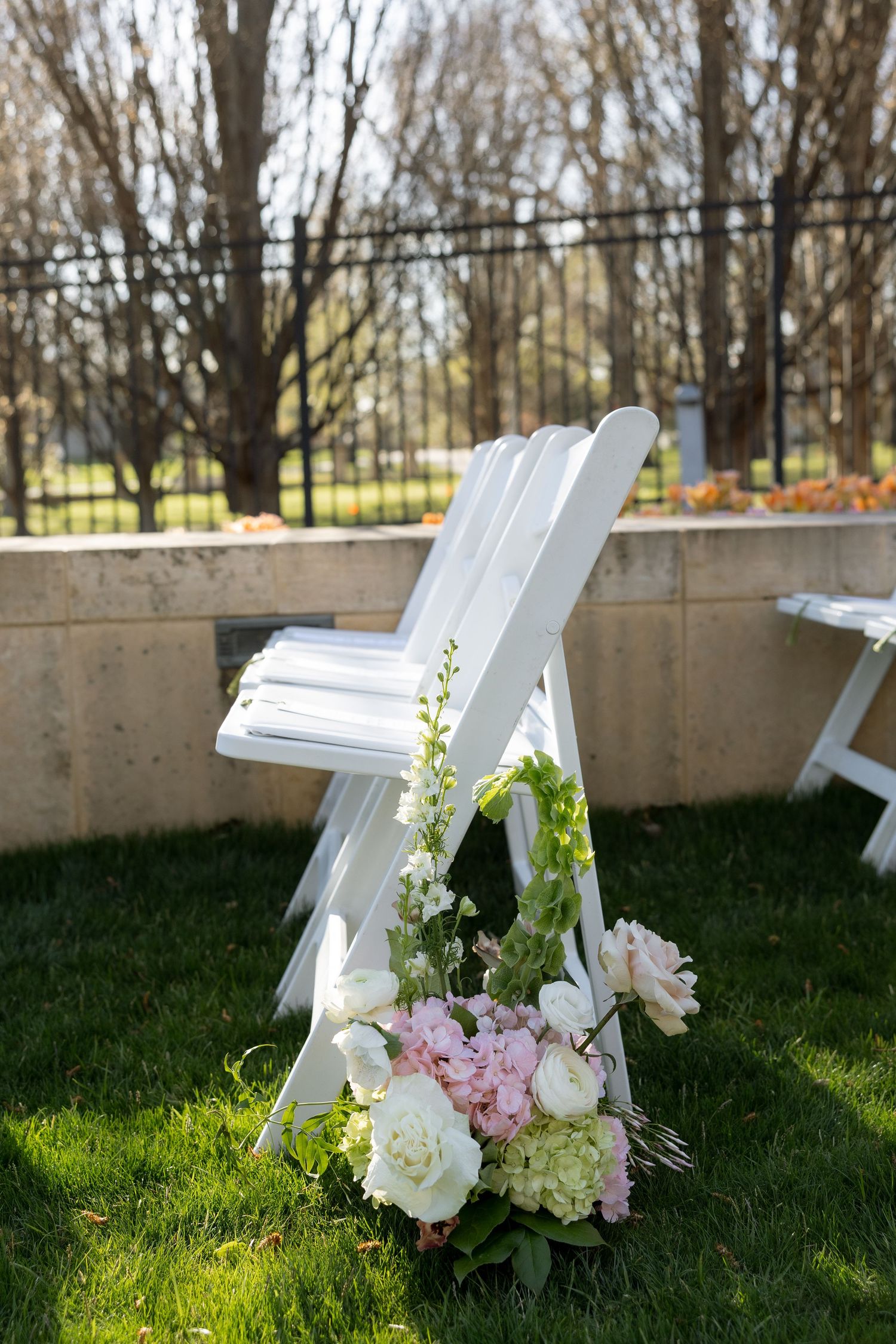 Pink and white floral bouquet rests against white folding chair on green grass.
