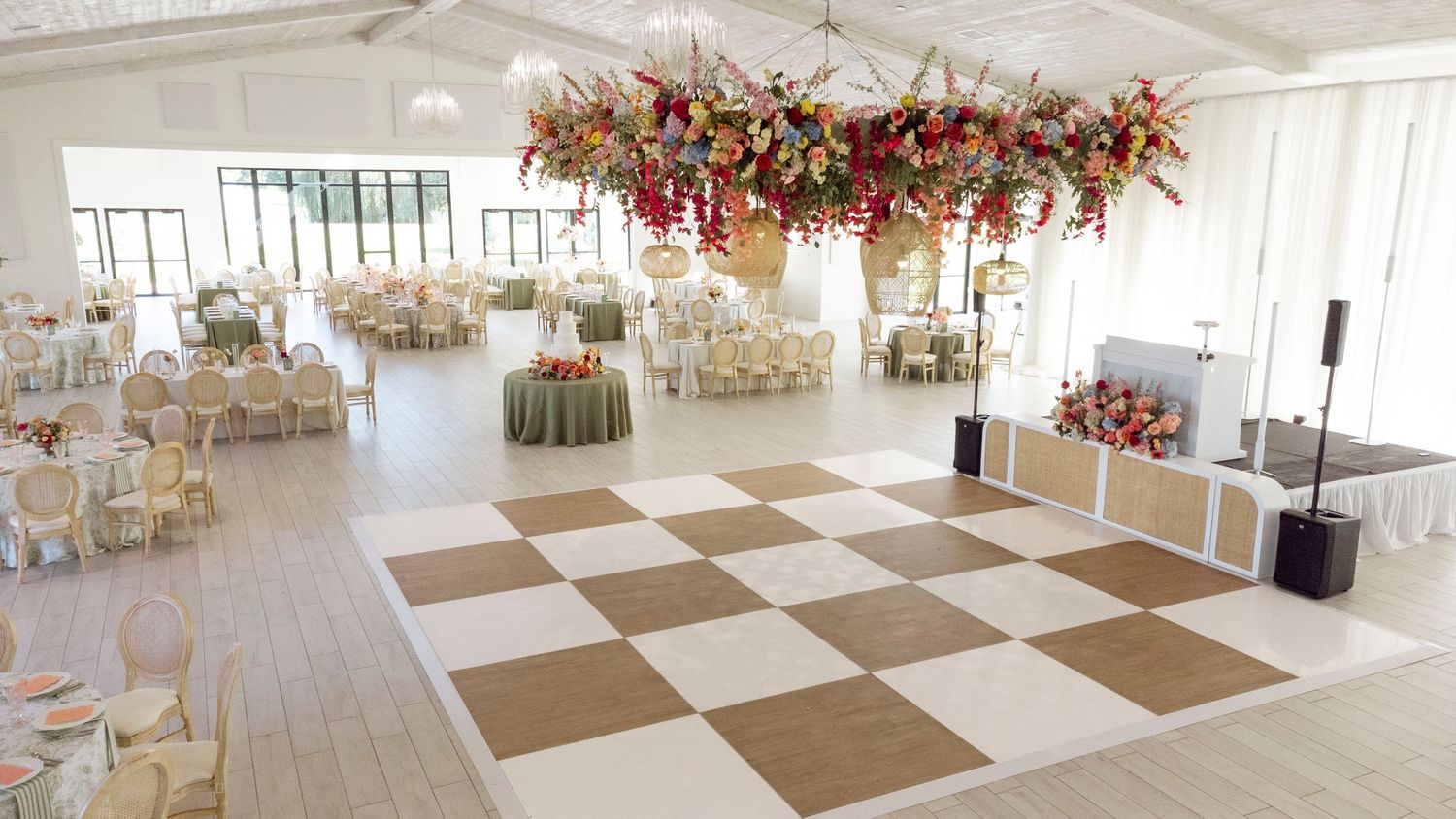 Spacious wedding venue with checkered floor and stunning floral chandelier installation.