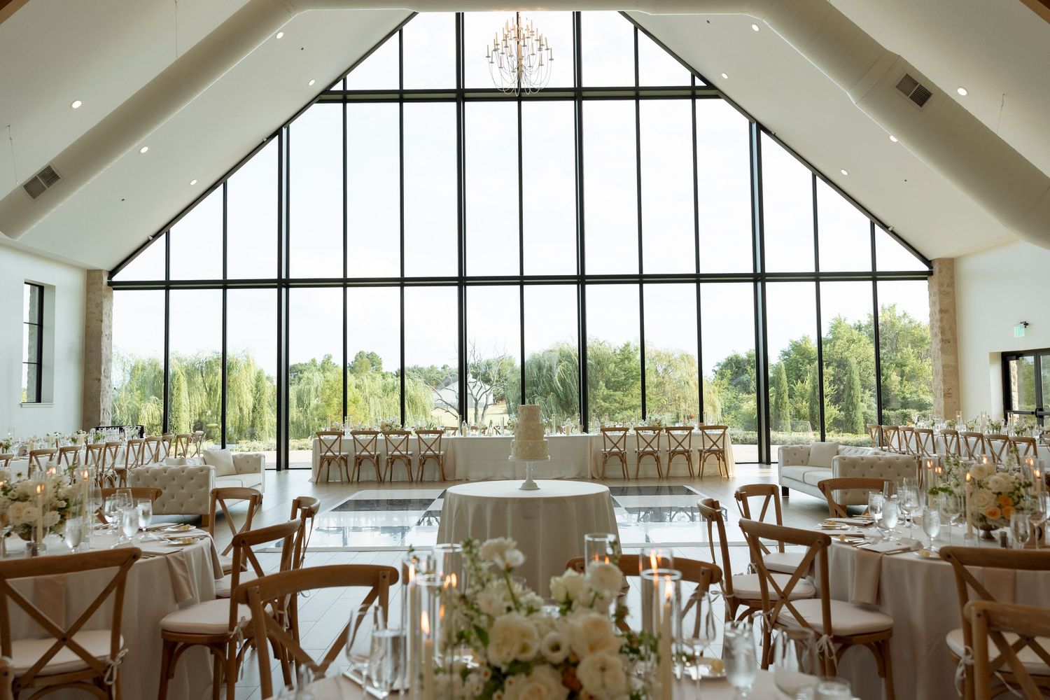 Elegant wedding reception venue with vaulted ceiling, white decor, and large arched windows overlooking scenic views.