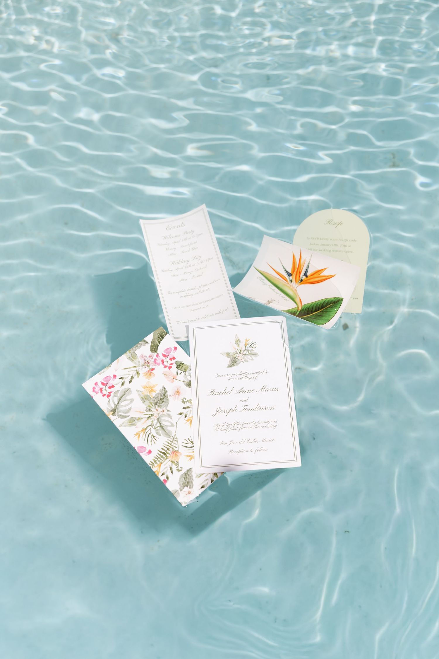 Elegant wedding invitation suite floating in clear blue pool water with floral accents.