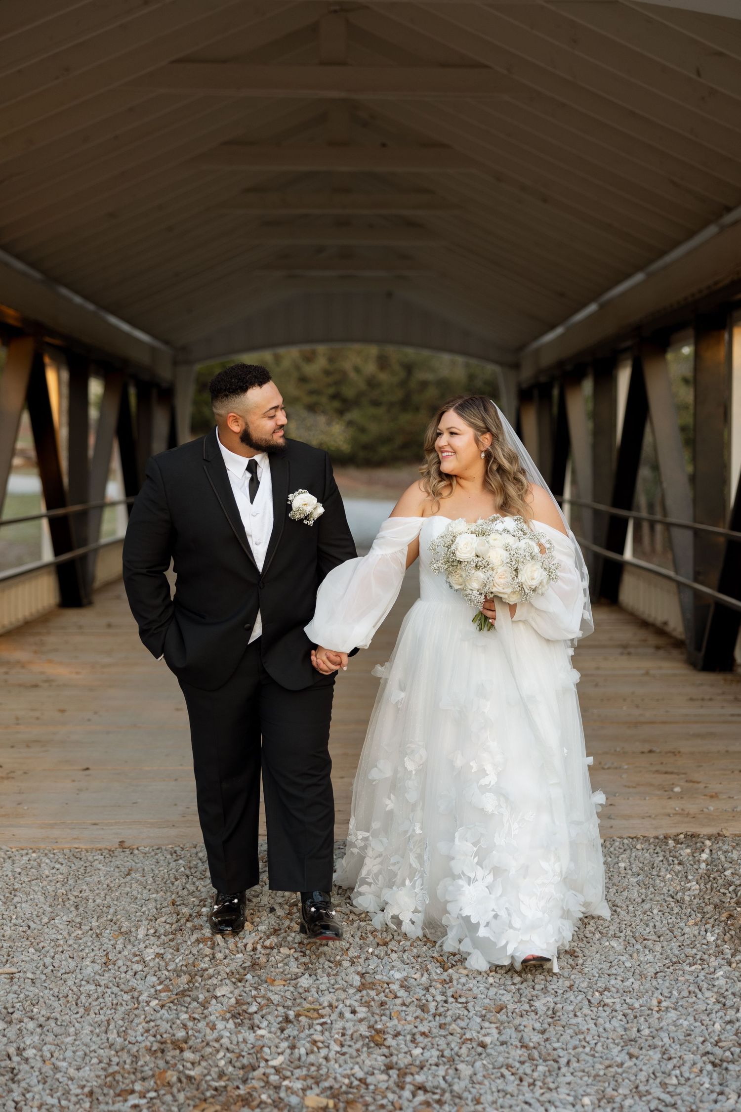 A casual wedding portrait of couple walking and laughing on wooden bridge.
