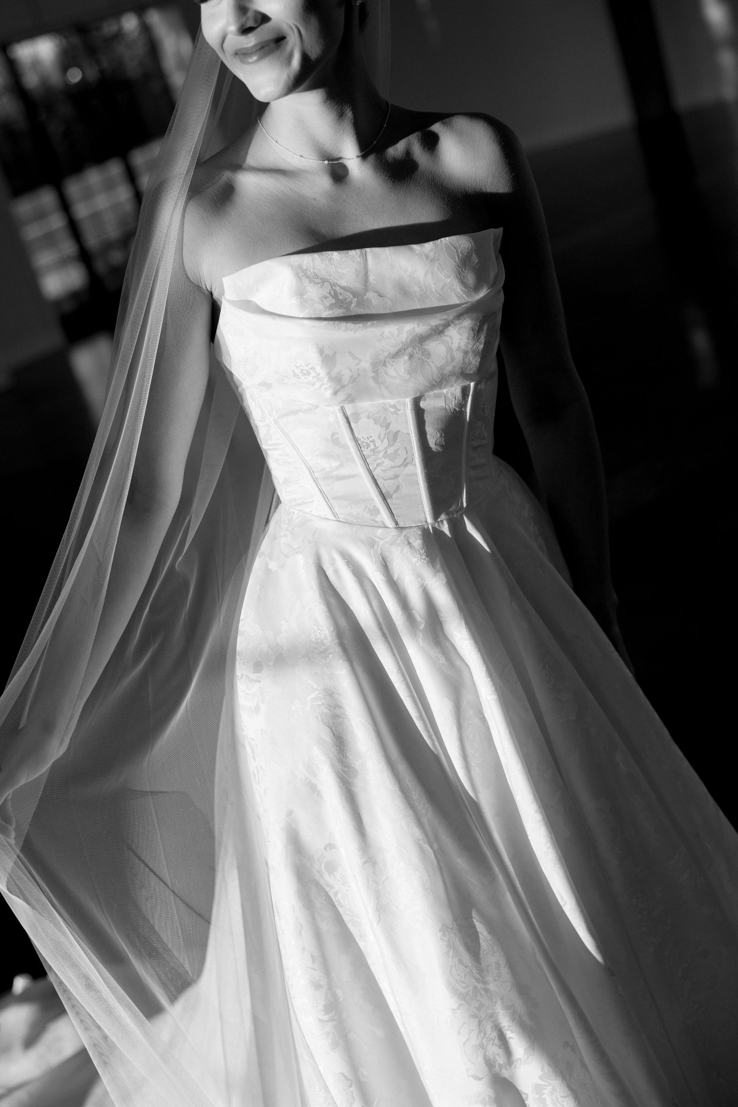Black and white photo of a strapless wedding dress with a flowing veil and structured bodice.