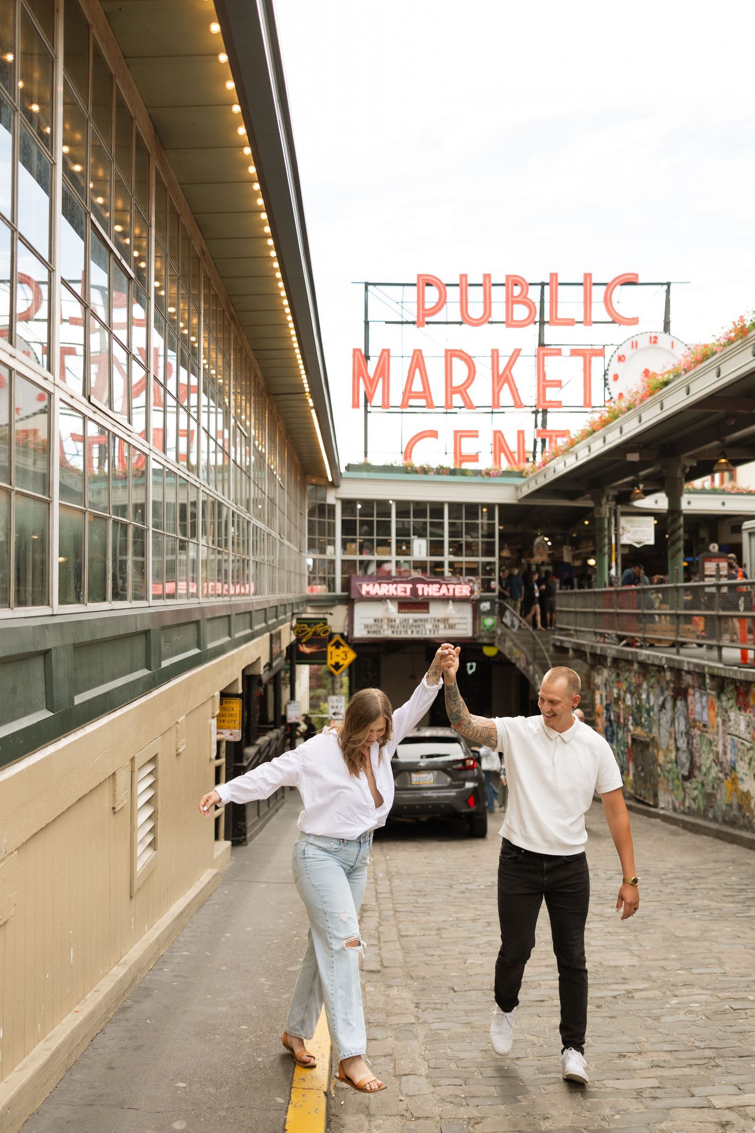 A couple holding hands and dancing beneath the iconic Pike Place Market sign in Seattle.
