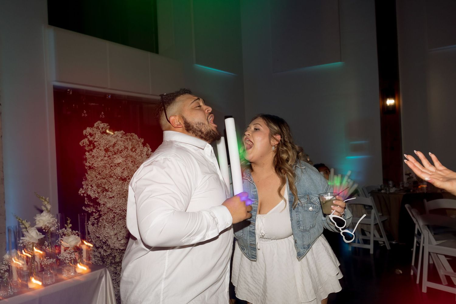 Couple dancing with glow sticks under colorful lighting at their wedding reception.
