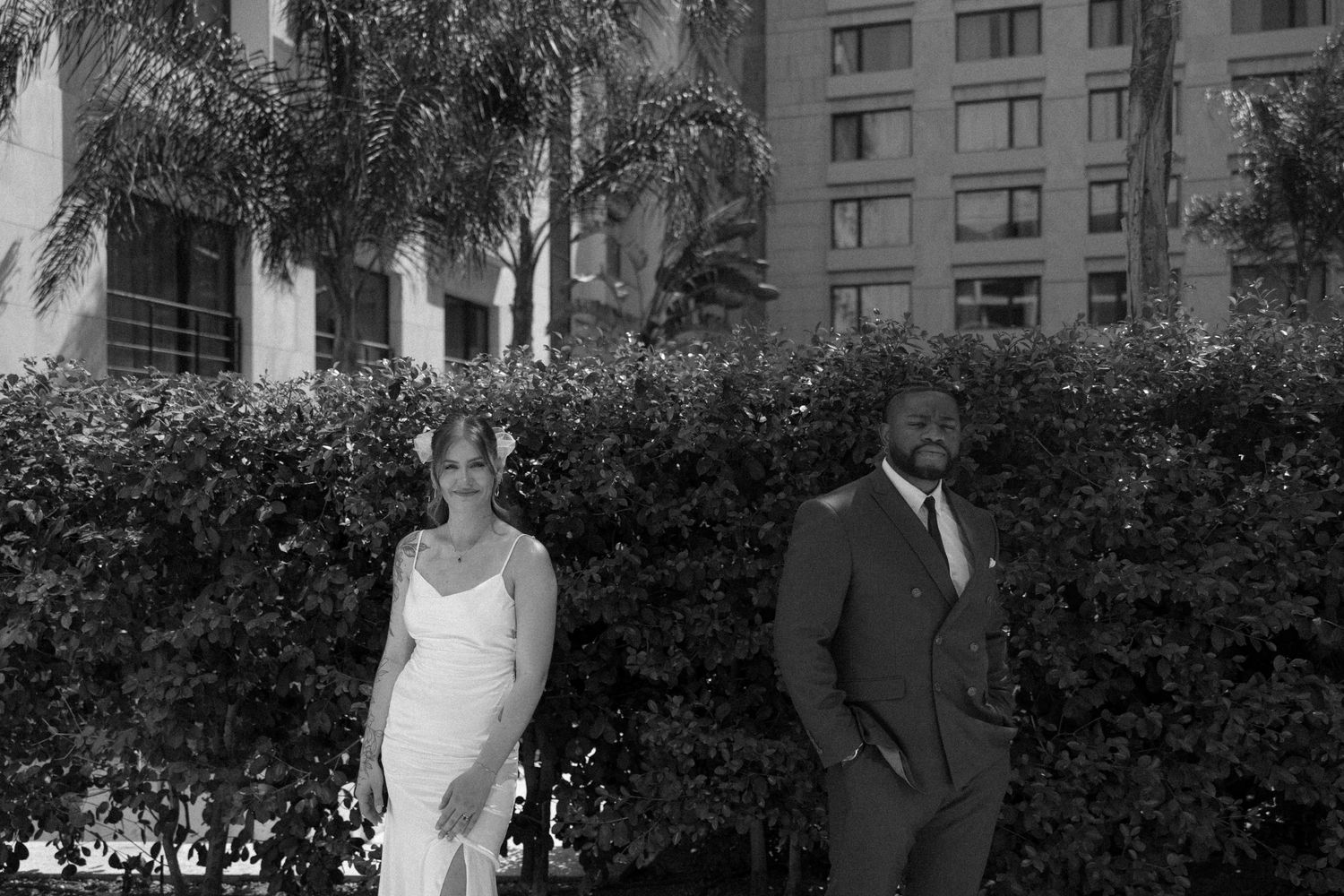 Black and white portrait of newlyweds standing by garden landscaping.