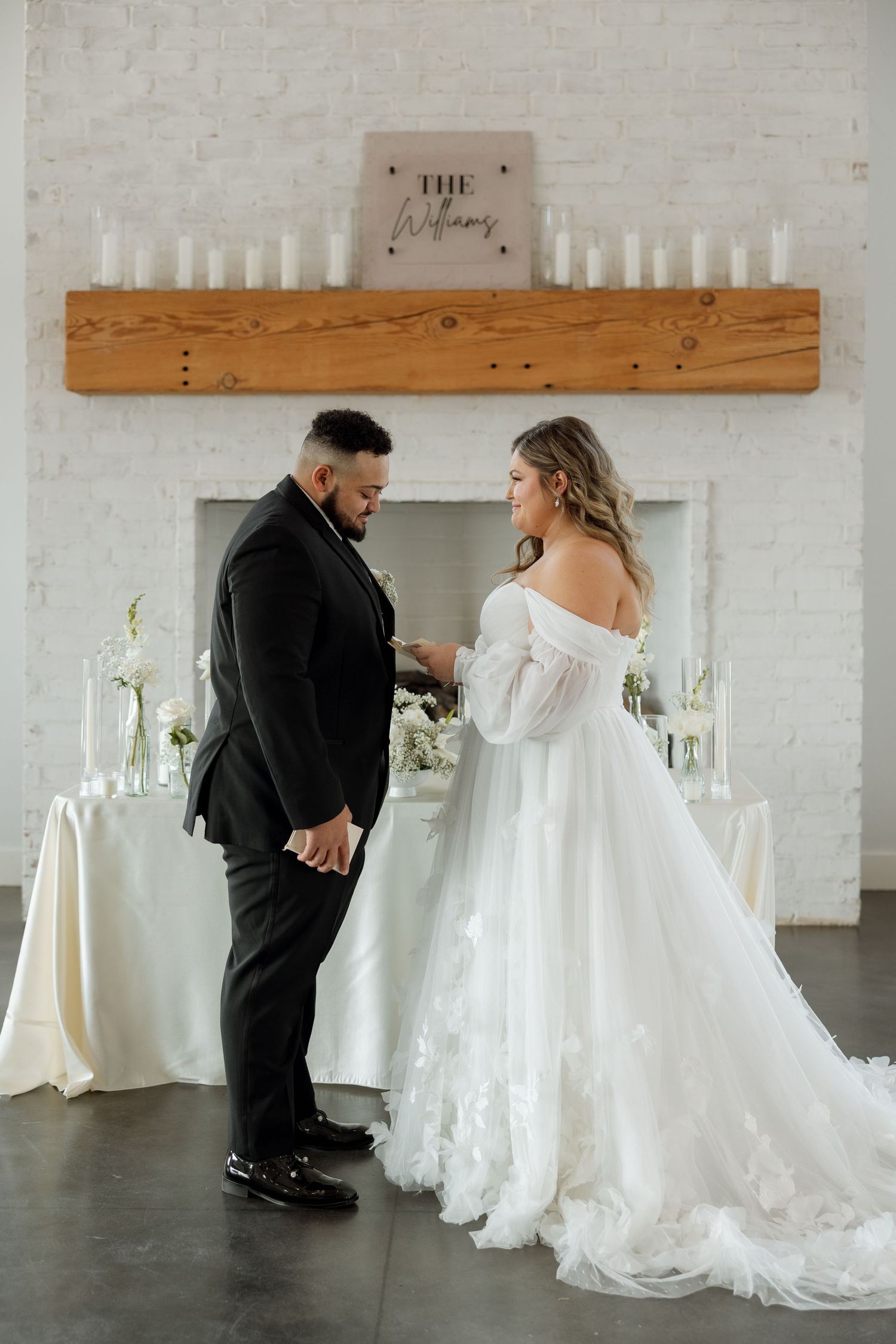 Couple shares private moment during indoor wedding ceremony beneath rustic wooden beam and candles.
