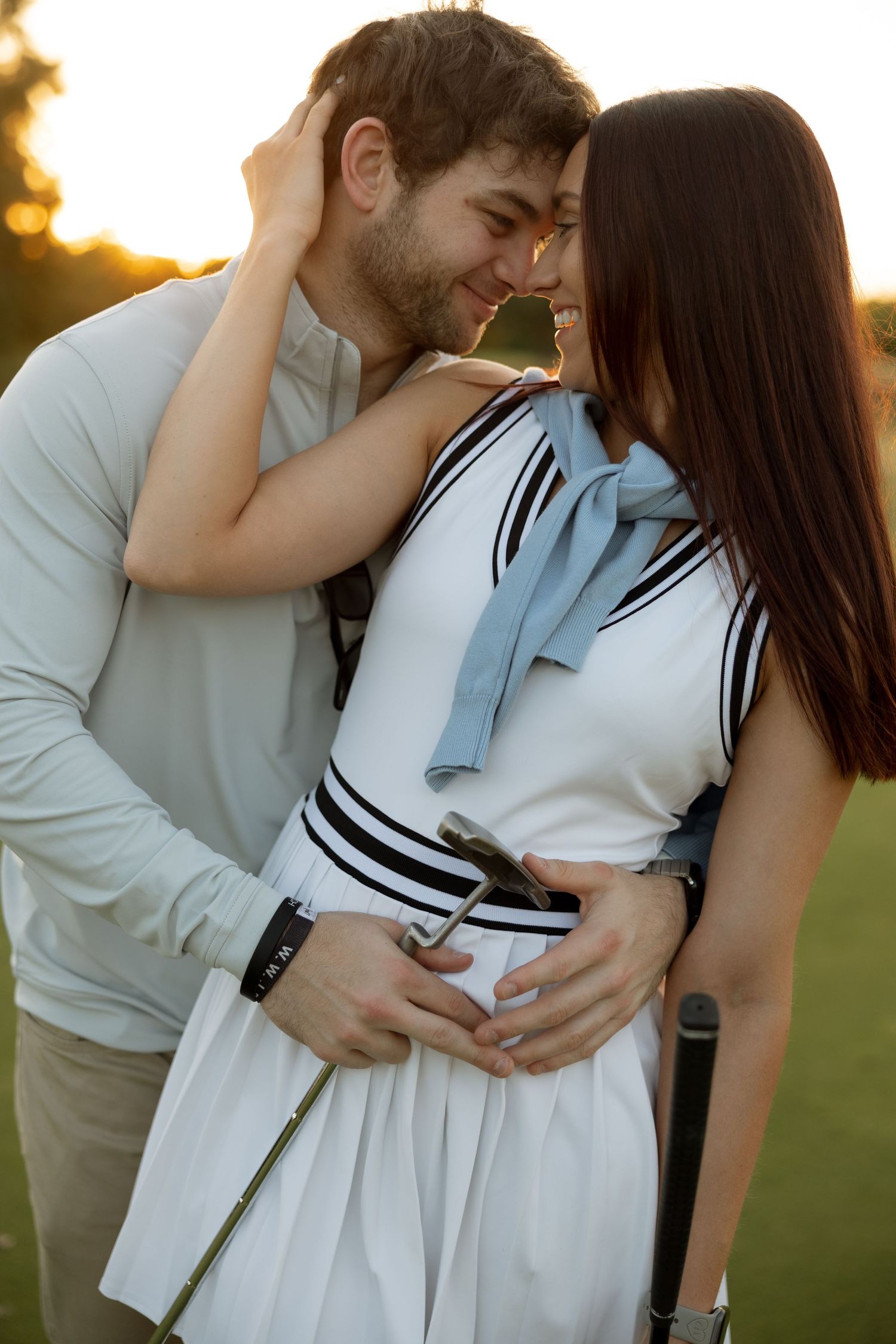 Intimate moment between couple in athletic wear on a golf course at sunset.