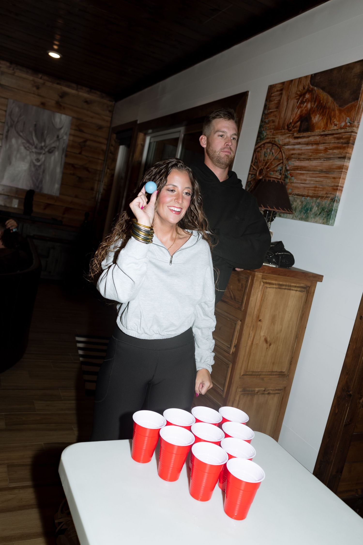 Person in casual attire preparing to throw a ping pong ball during a drinking game.