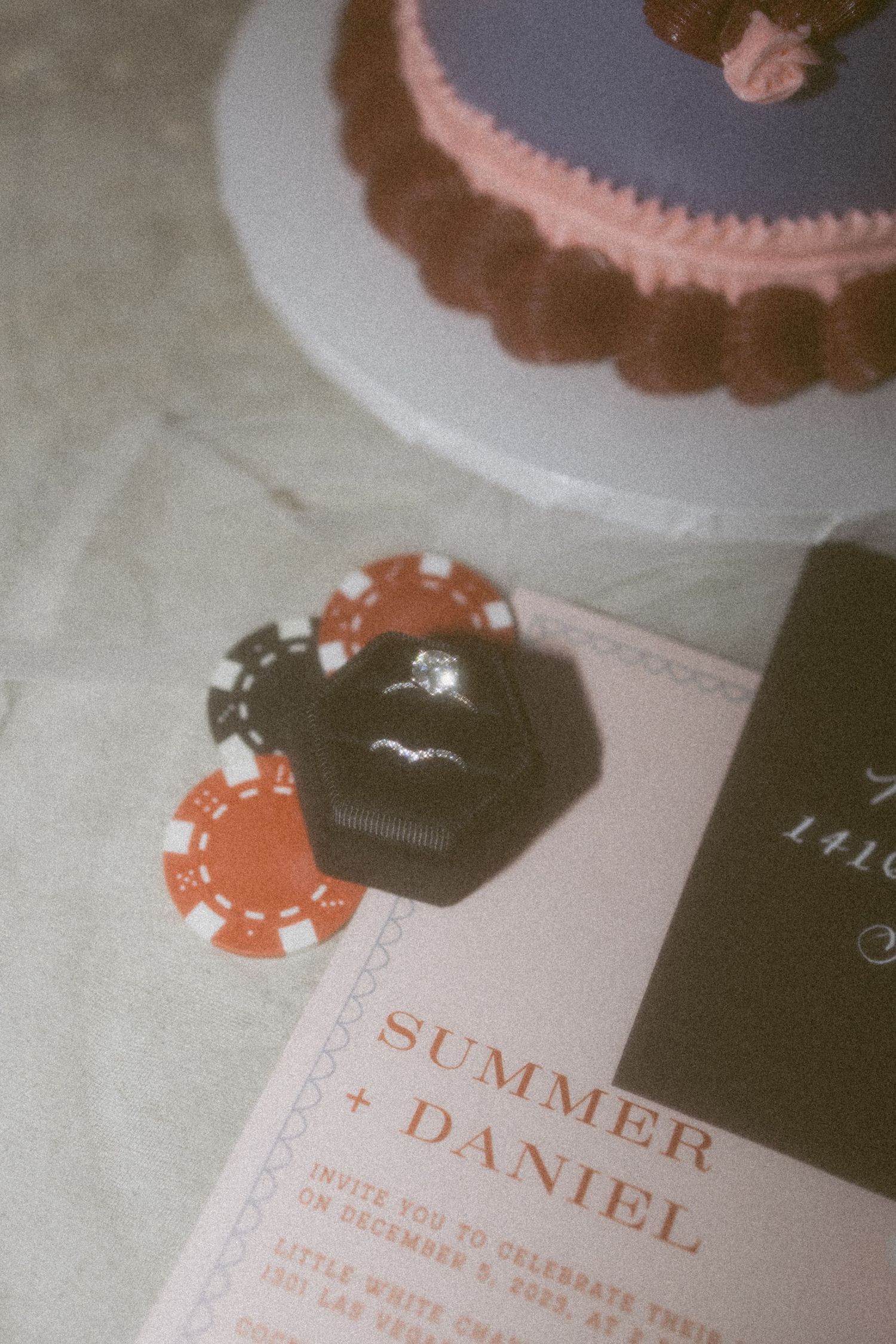 Close-up of a wedding invitation with poker chips and cake in soft focus.