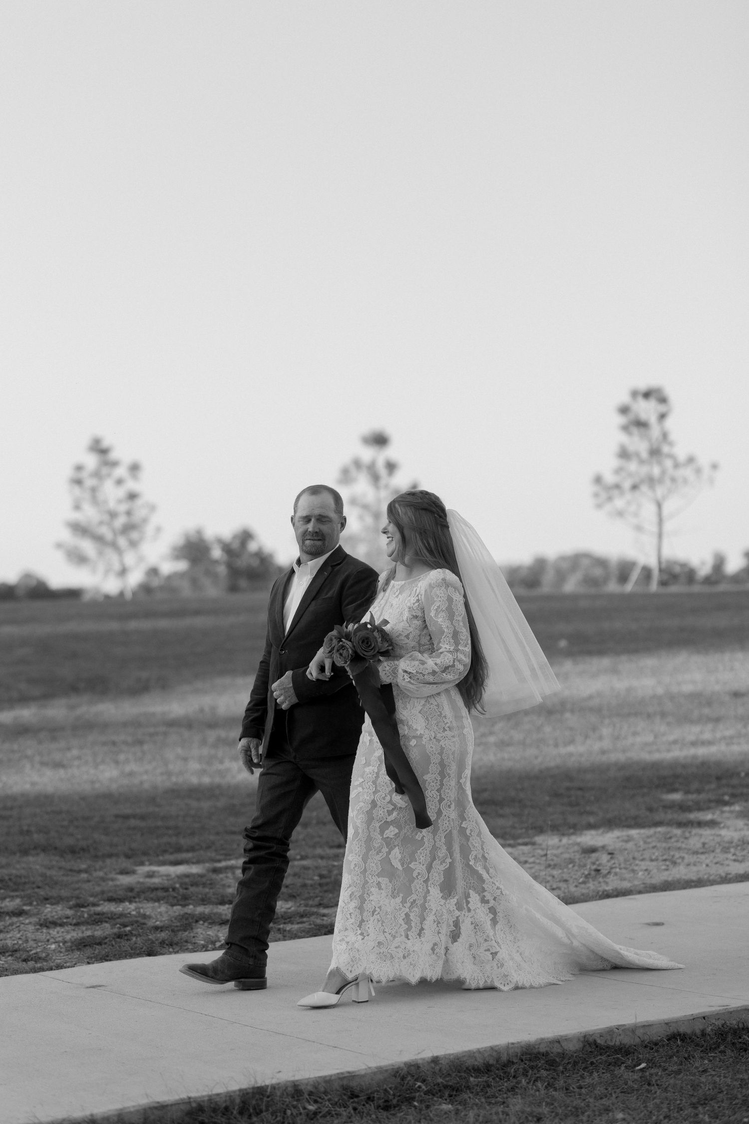 Black and white portrait of couple walking on outdoor path in formal attire.