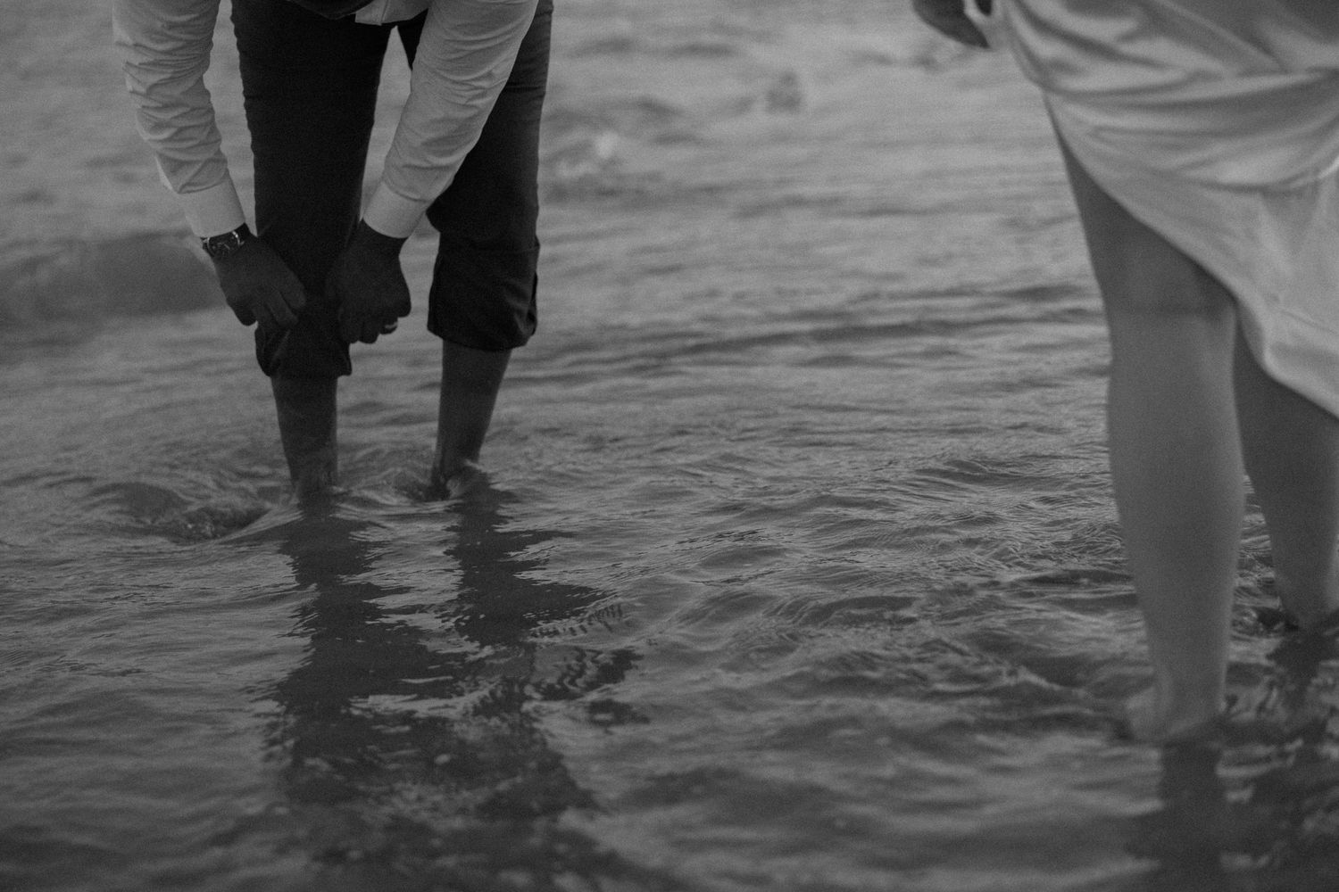 Black and white photo of two people standing ankle-deep in ocean water.