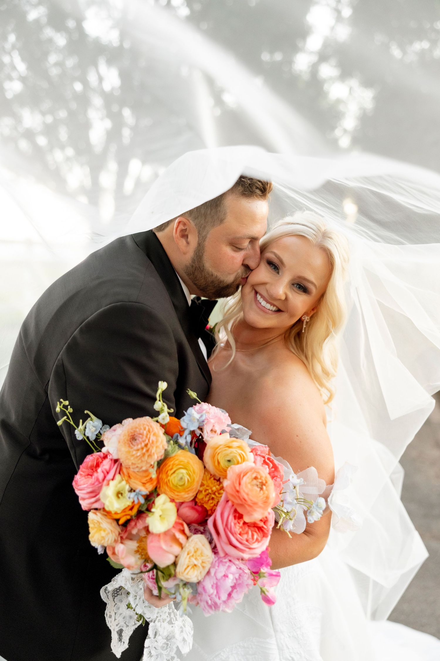 Intimate wedding moment captured with soft lighting and vibrant peach and pink floral bouquet.