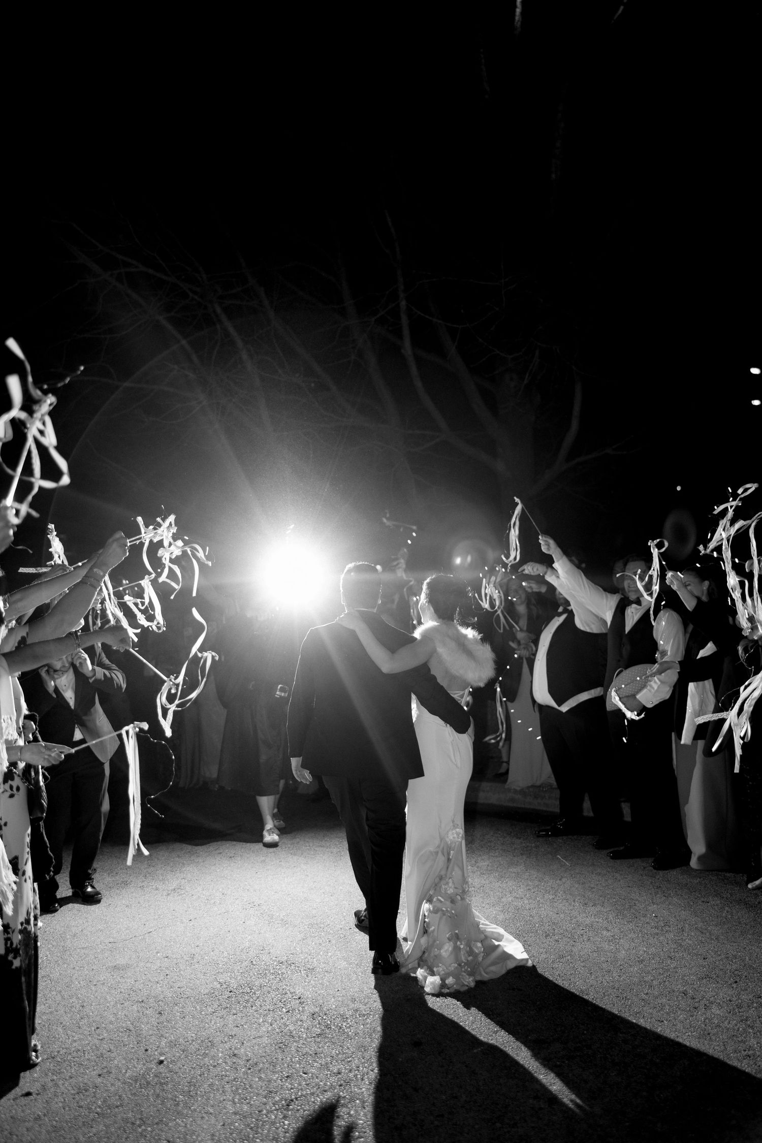 Black and white photo of bride and groom kissing during a sparkler send-off at night.