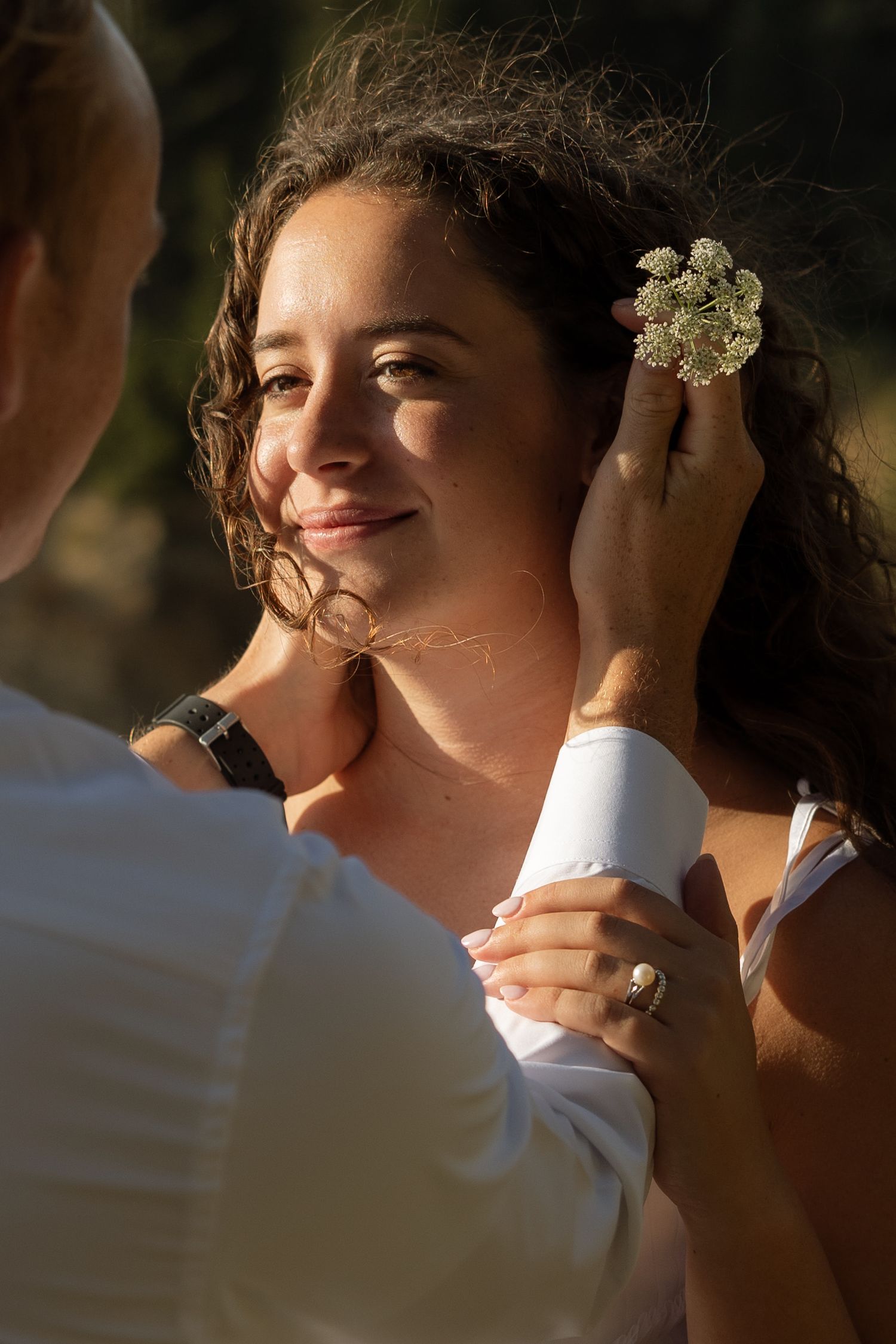 A tender moment captured as a flower is placed in wavy hair during a coastal wedding.