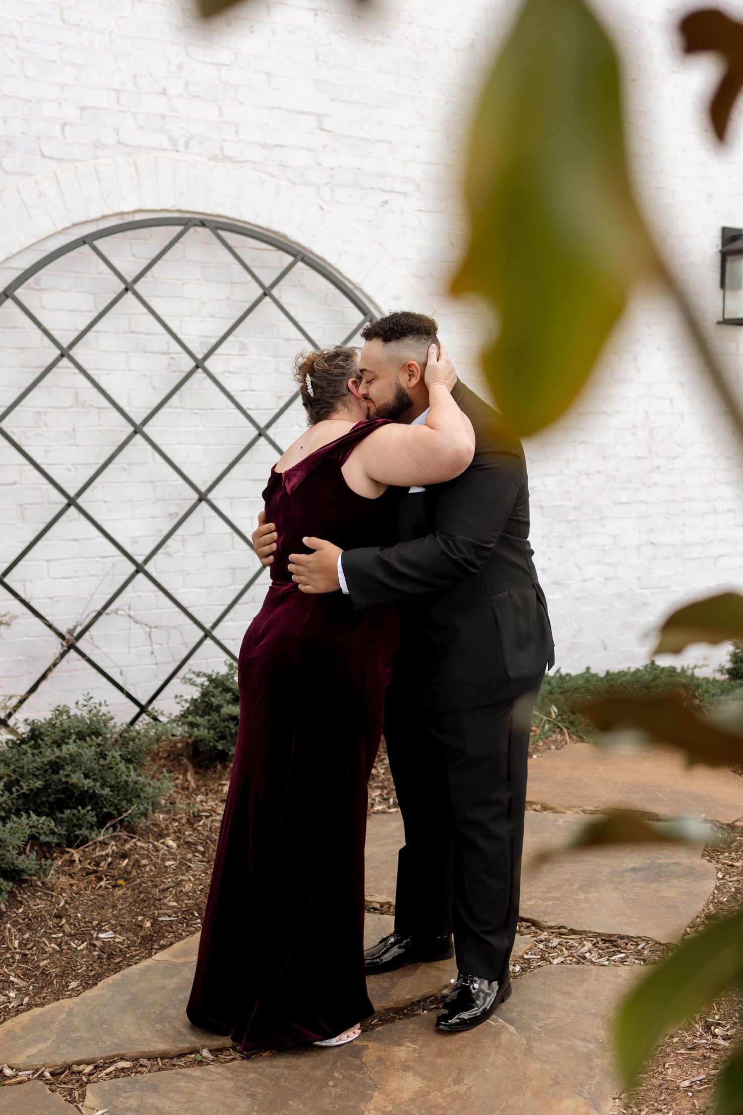 A romantic embrace against a white wall with decorative lattice.
