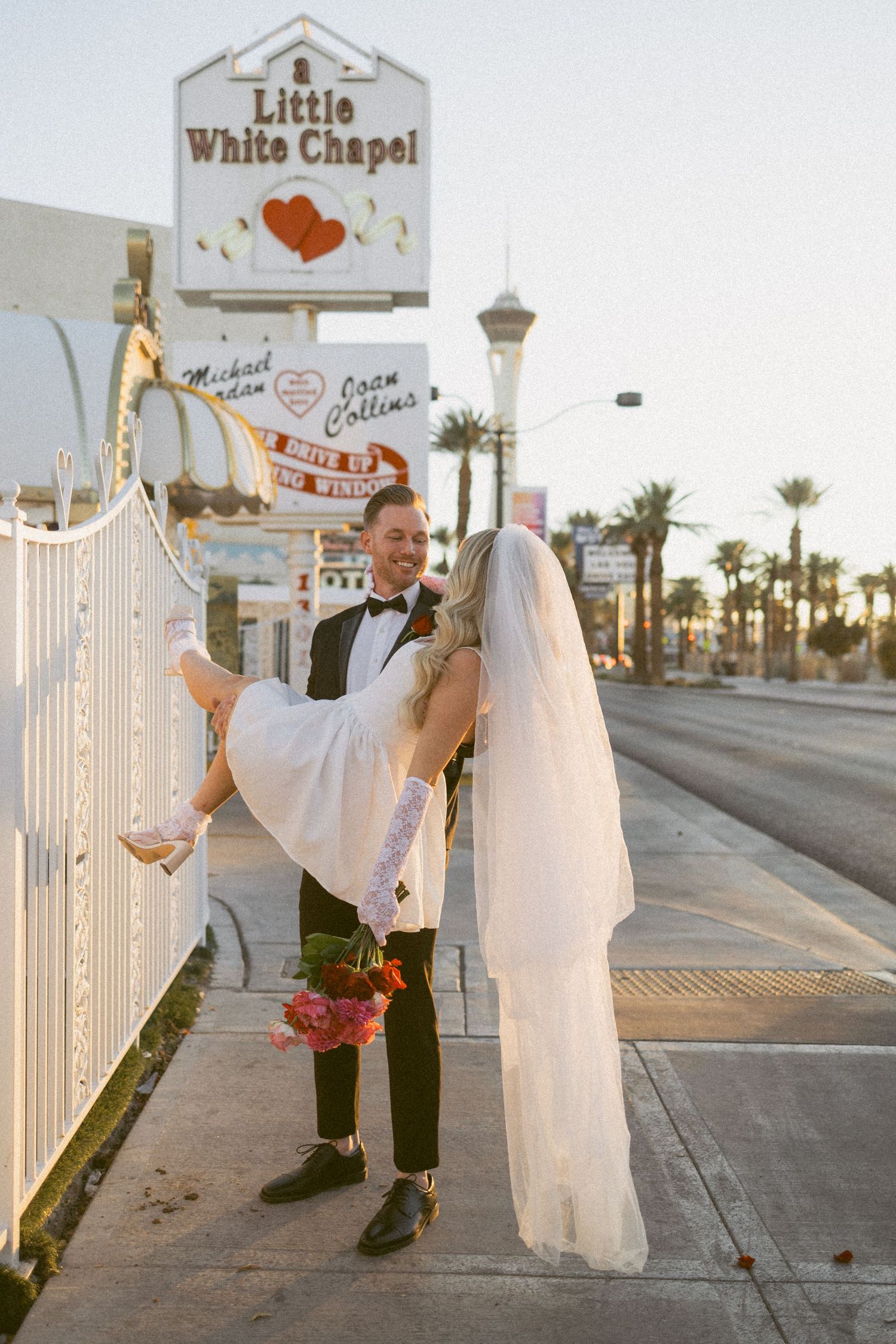 A romantic wedding photo outside the Little White Chapel with the Las Vegas Stratosphere tower visible.